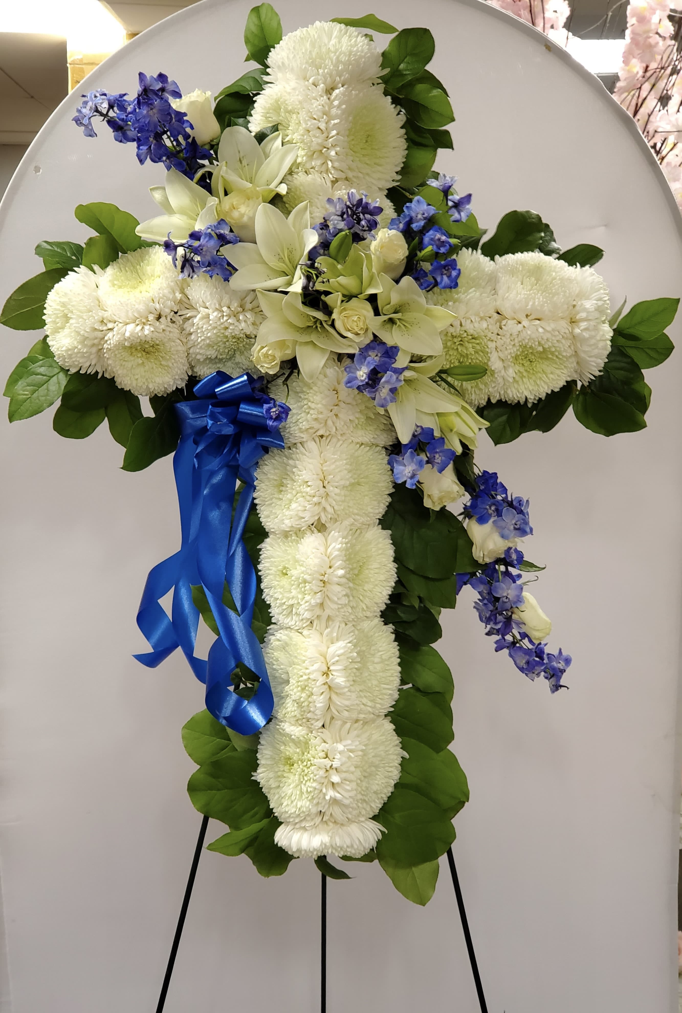 White floral cross arrangement with blue ribbon on an easel