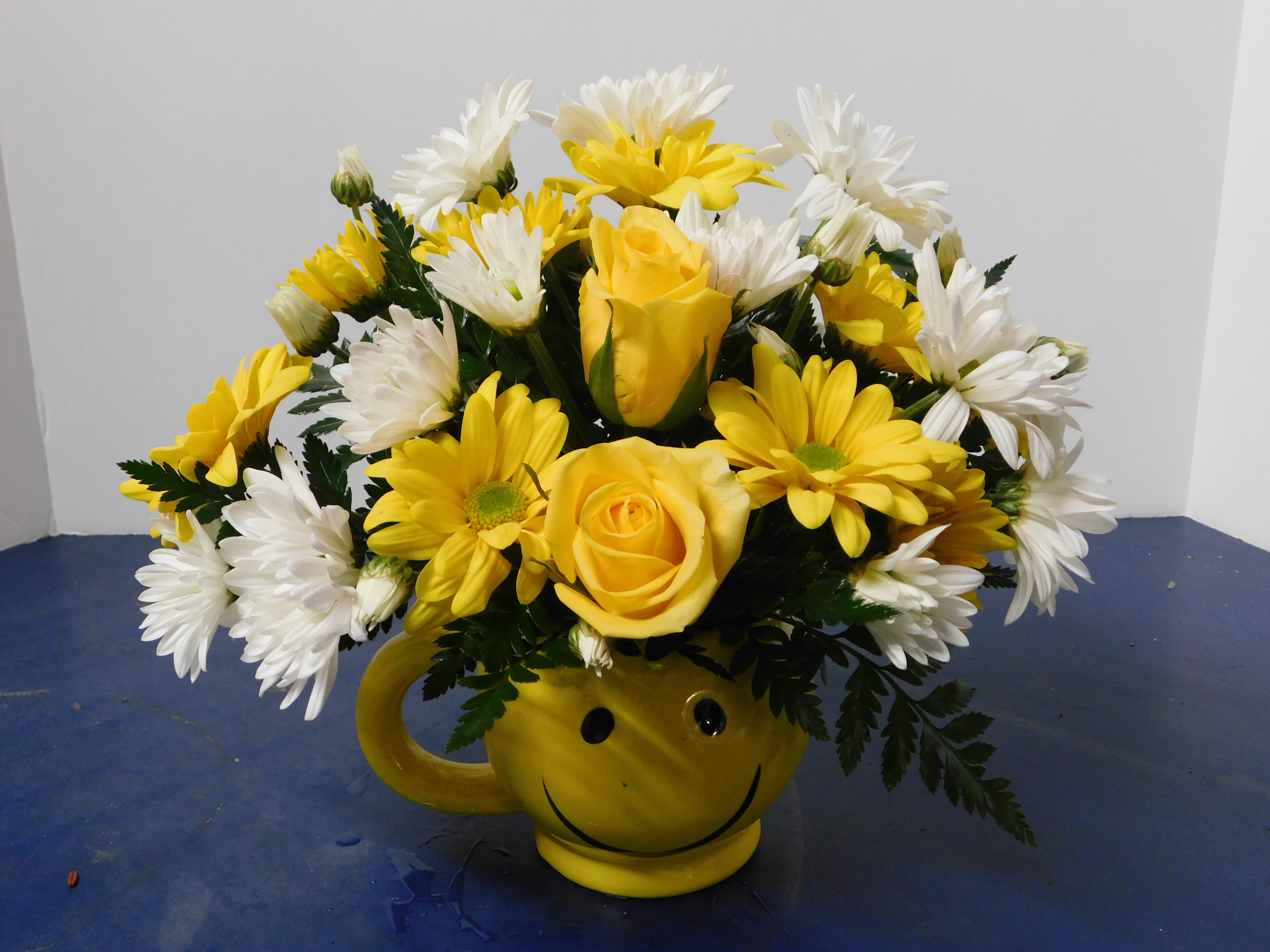 Yellow roses and white daisies in a smiley-face mug