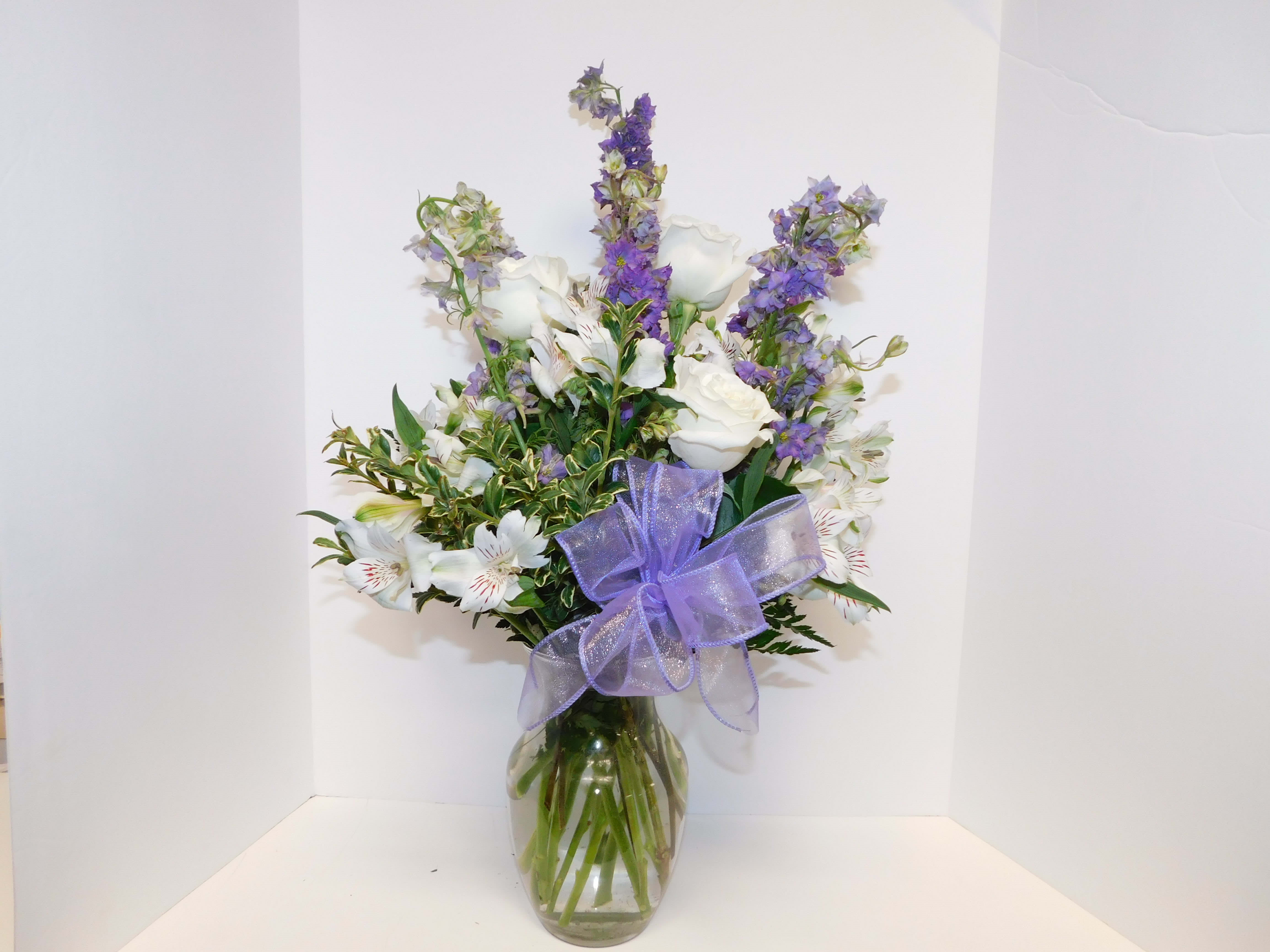 White and purple flower arrangement in a glass vase with a lavender bow