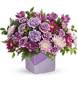 Purple mixed flower arrangement in a lavender square vase