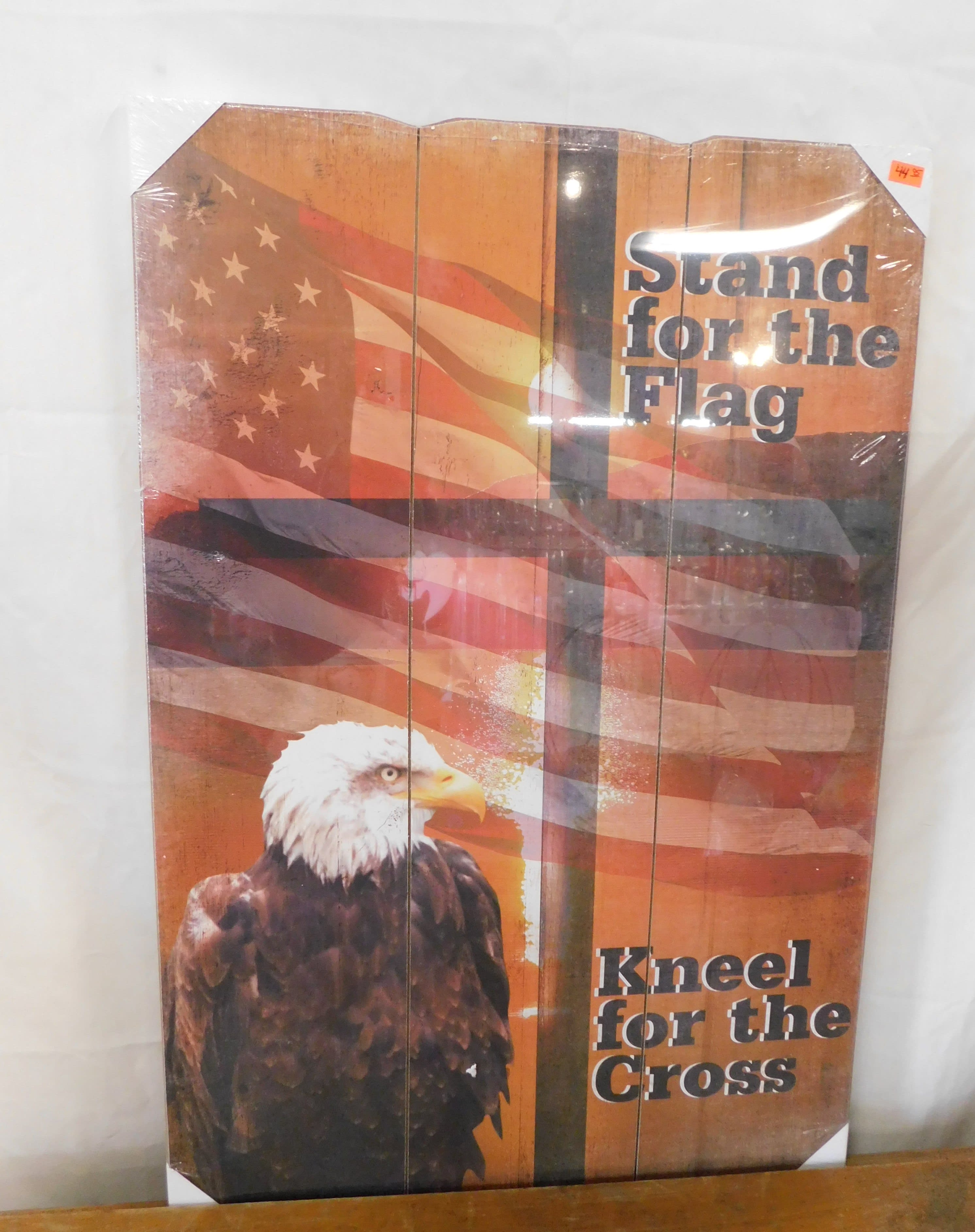 Decorative sign with an American flag and eagle, reading "Stand for the Flag" and "Kneel for the Cross".