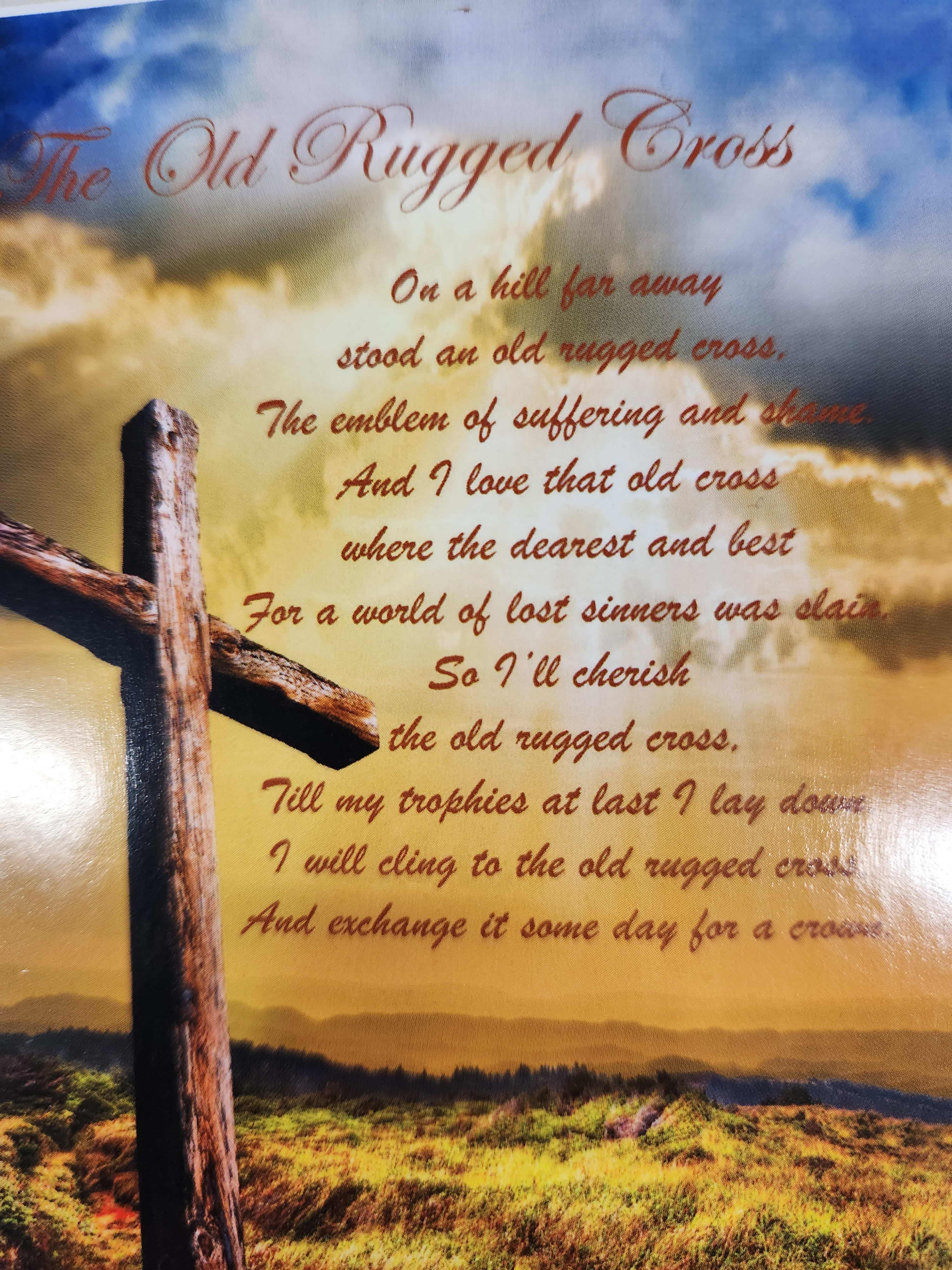 A printed memorial poem with a wooden cross against a cloudy sky