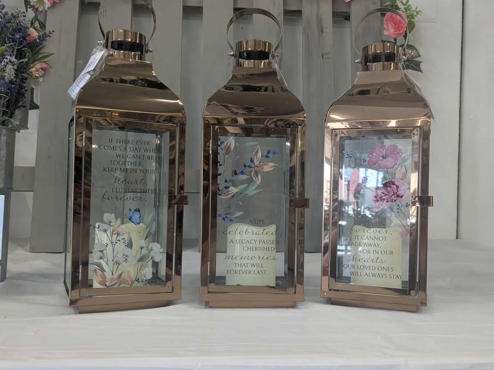 Three rose-gold lanterns with floral inserts and memorial quotes