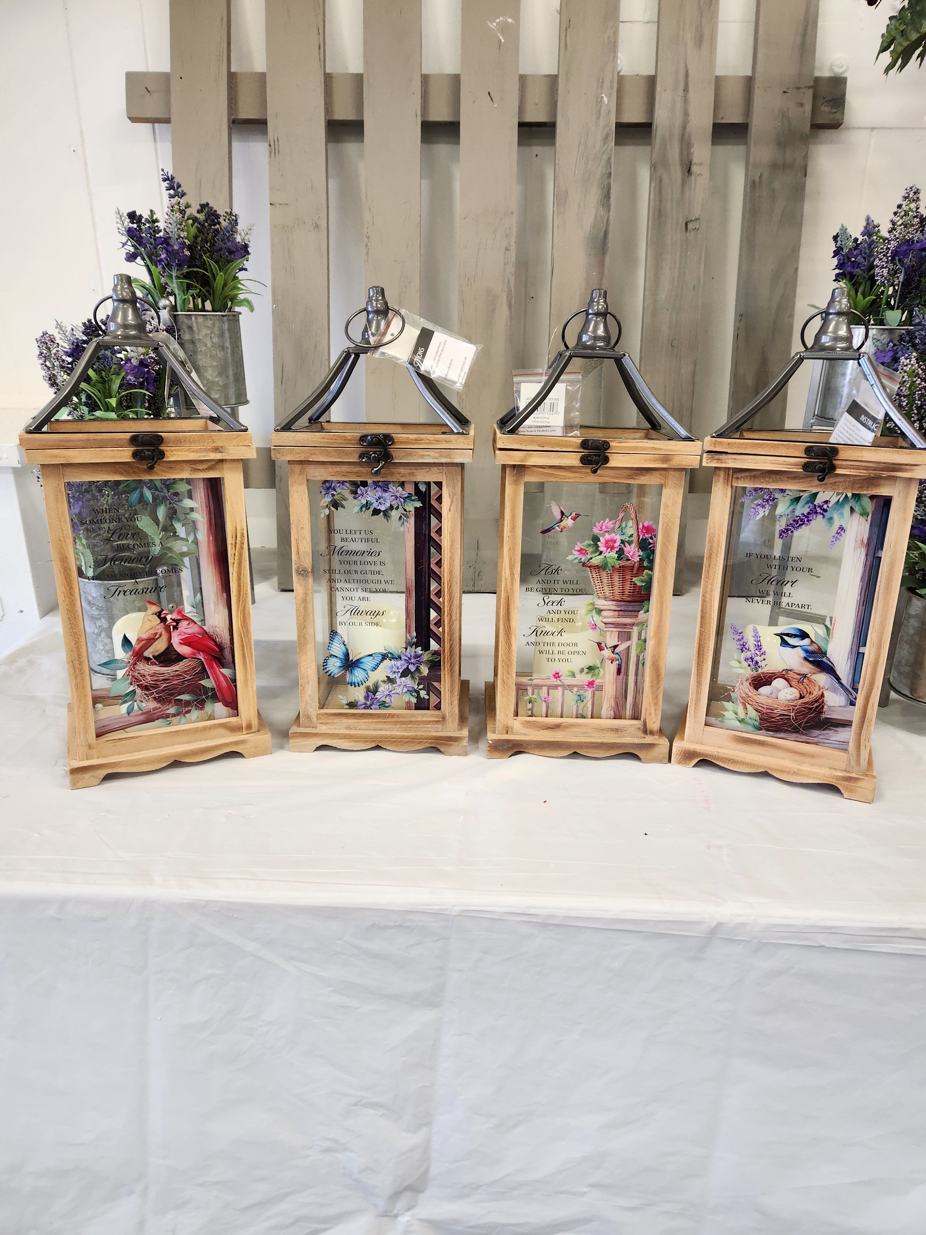 Four wooden lanterns with floral prints and small purple flower arrangements