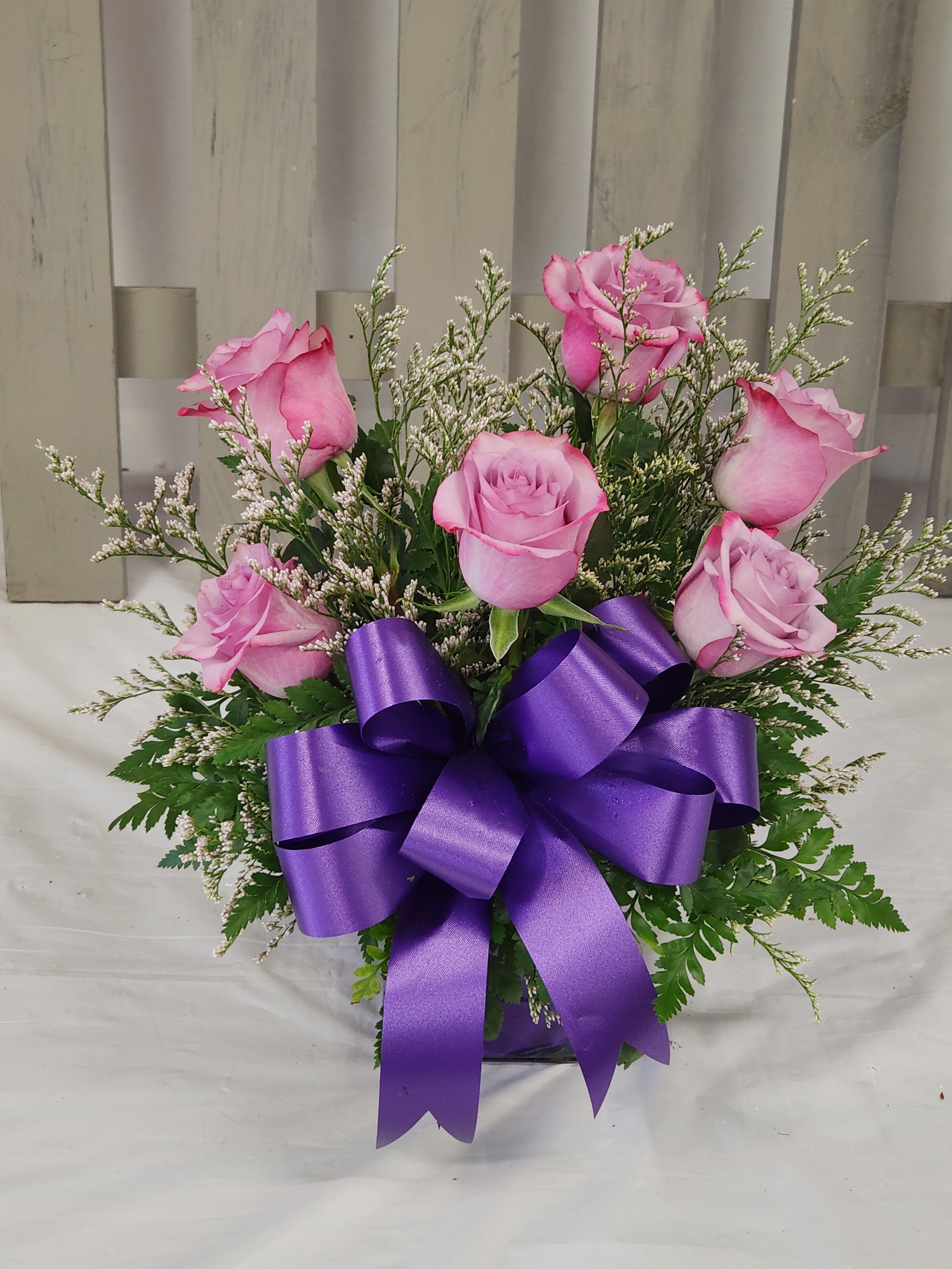 Pink roses arranged with a purple ribbon bow
