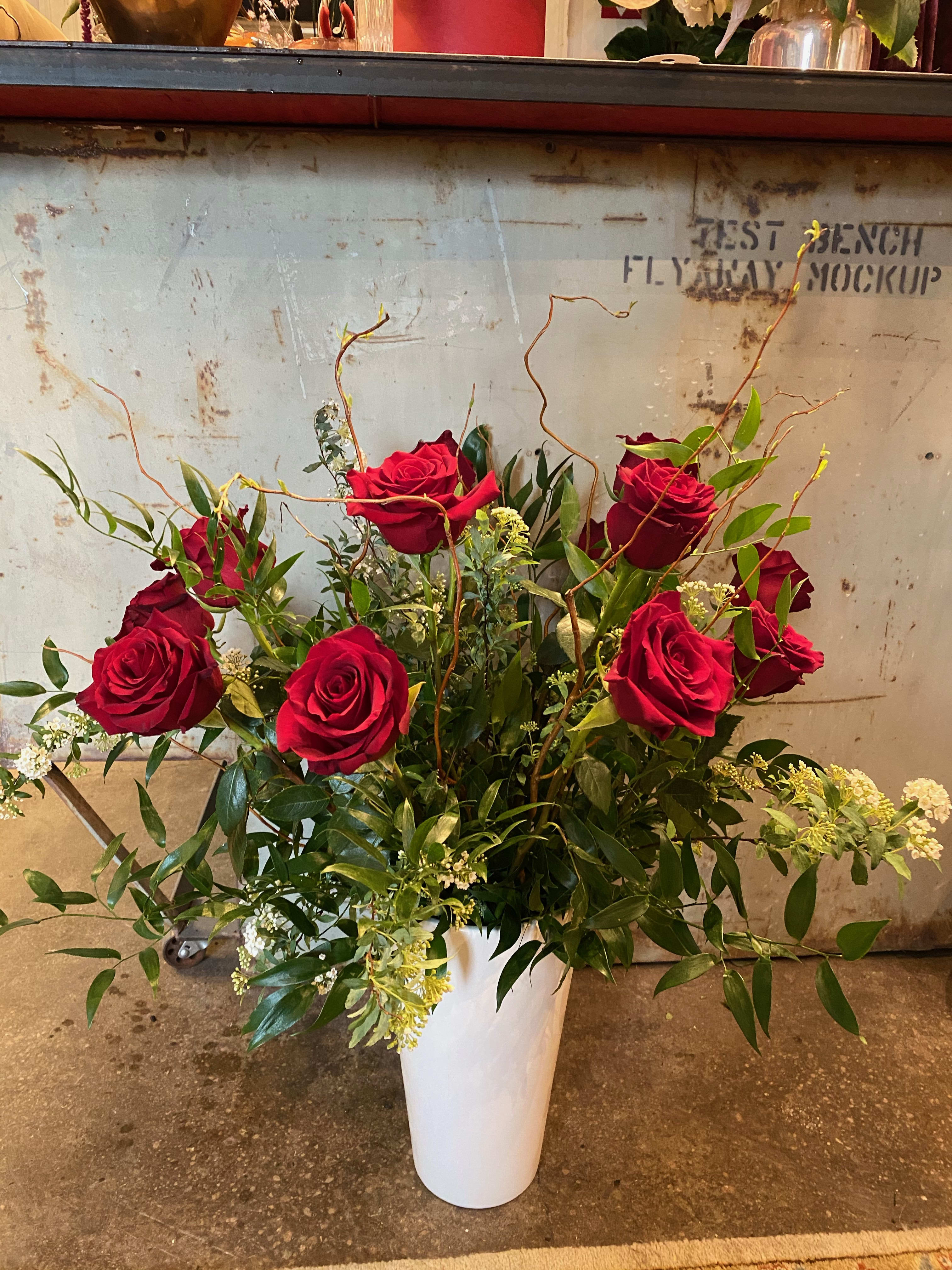 Red roses arranged in a white vase with greenery