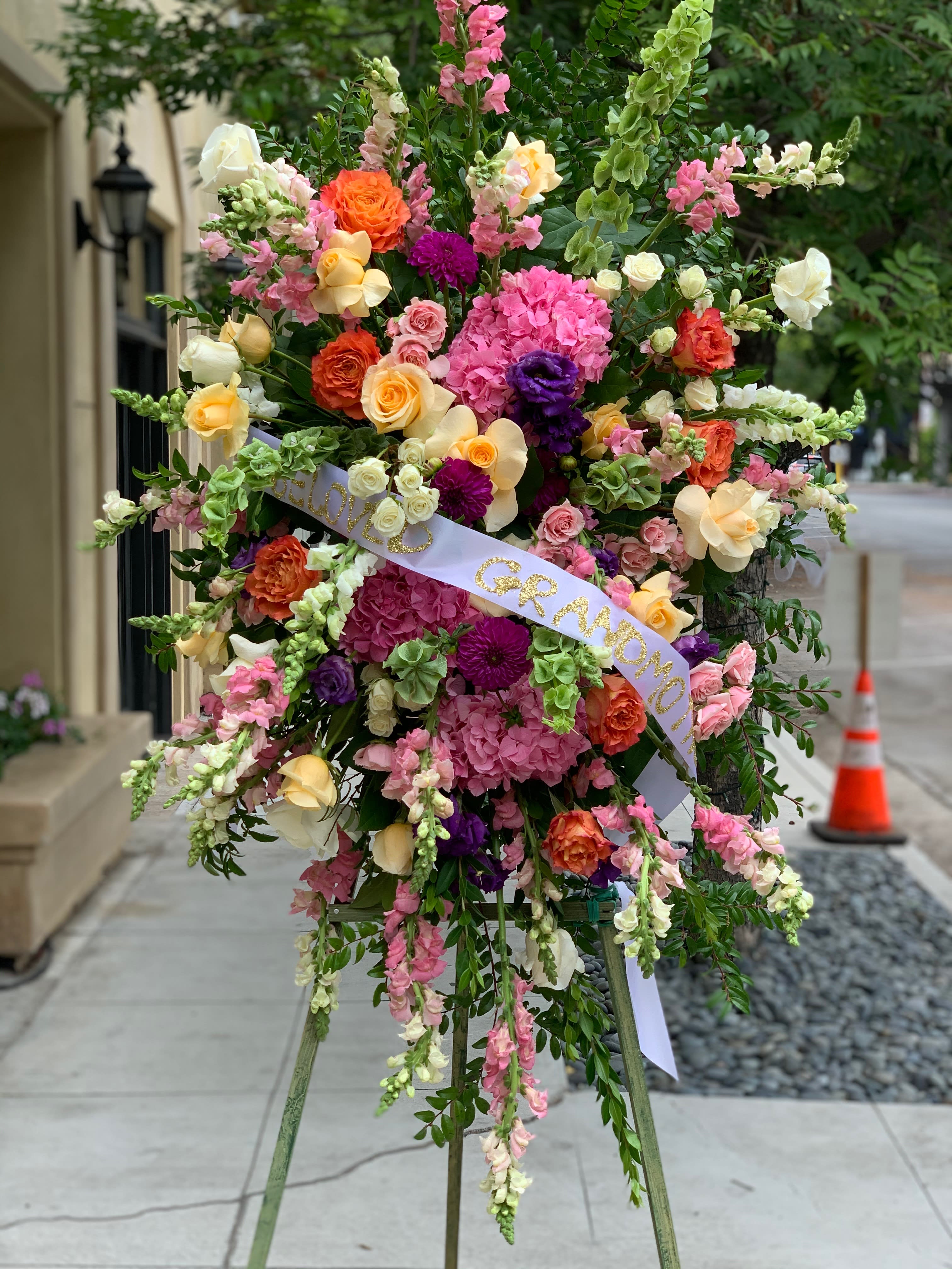 Large standing floral spray with pink, orange, yellow, and white blooms on an easel.