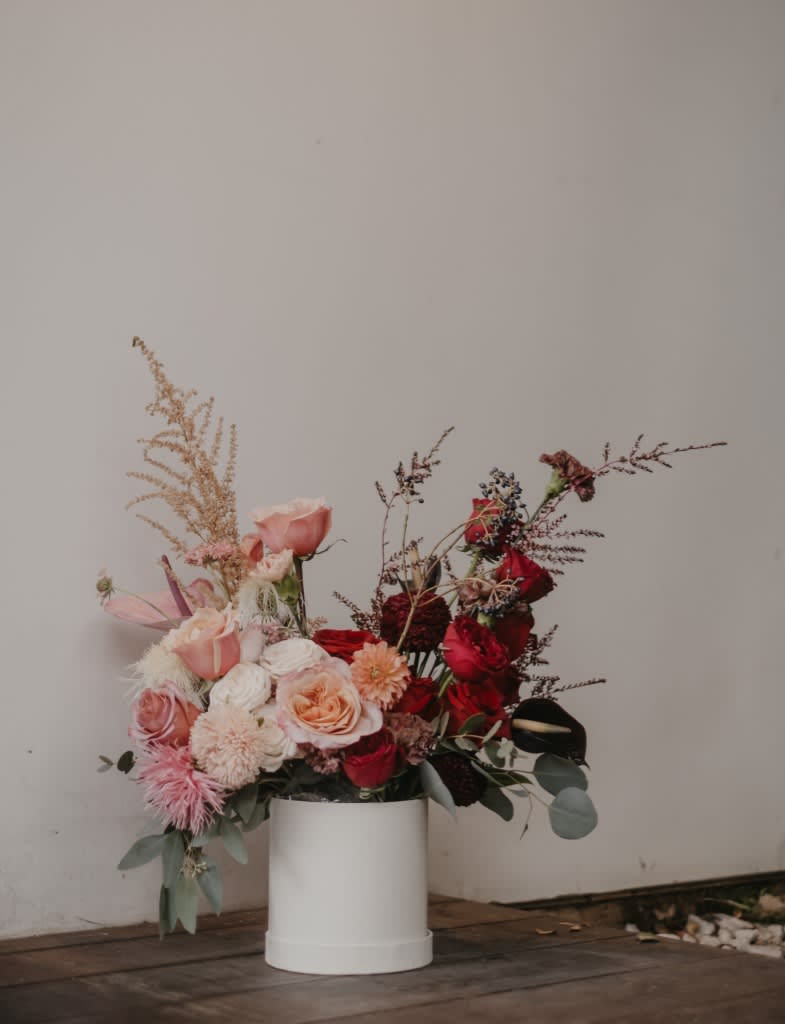 Pink and red rose arrangement in a white cylindrical vase
