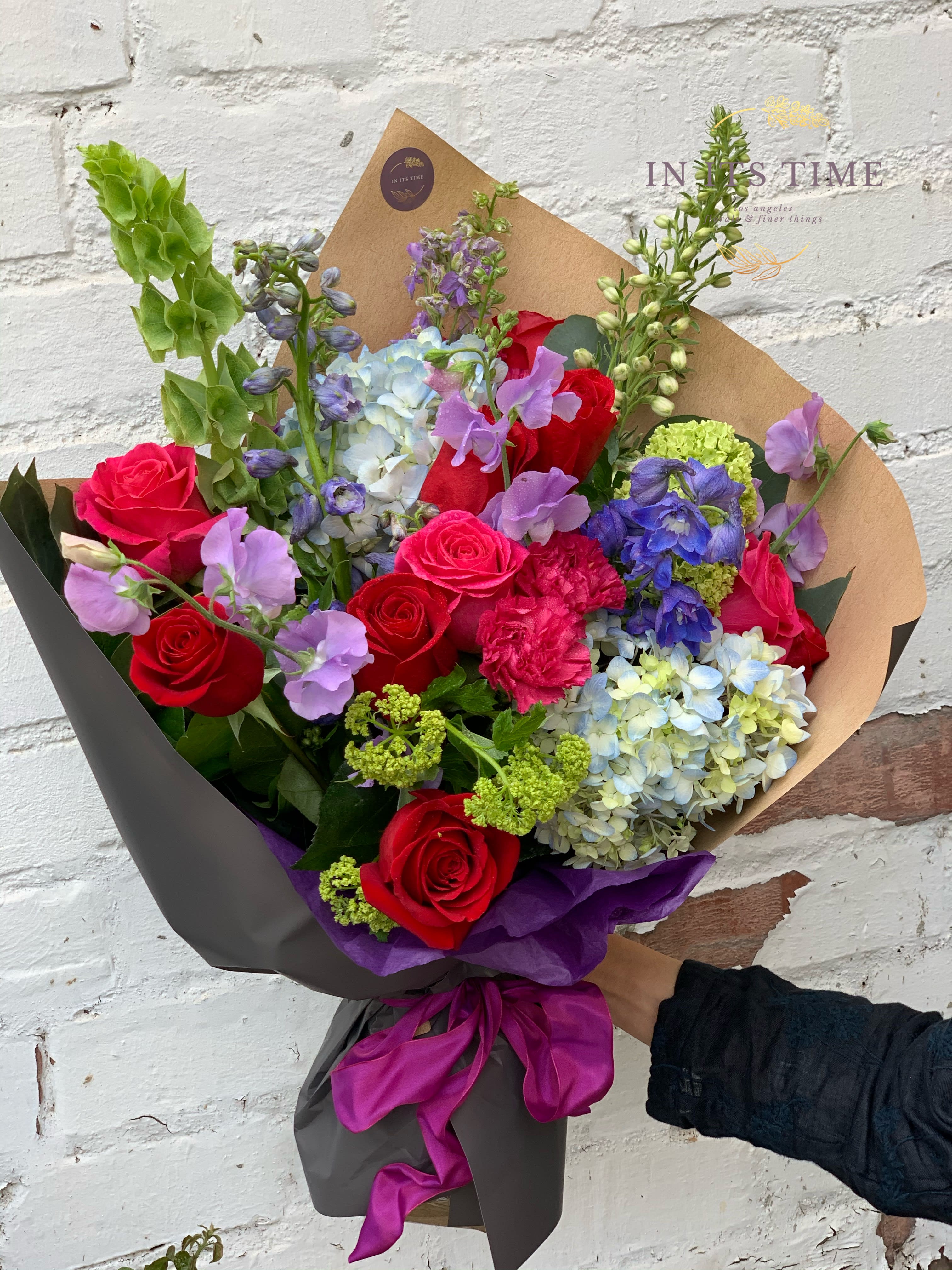 Bouquet of red roses, blue hydrangeas, and purple flowers wrapped in brown paper