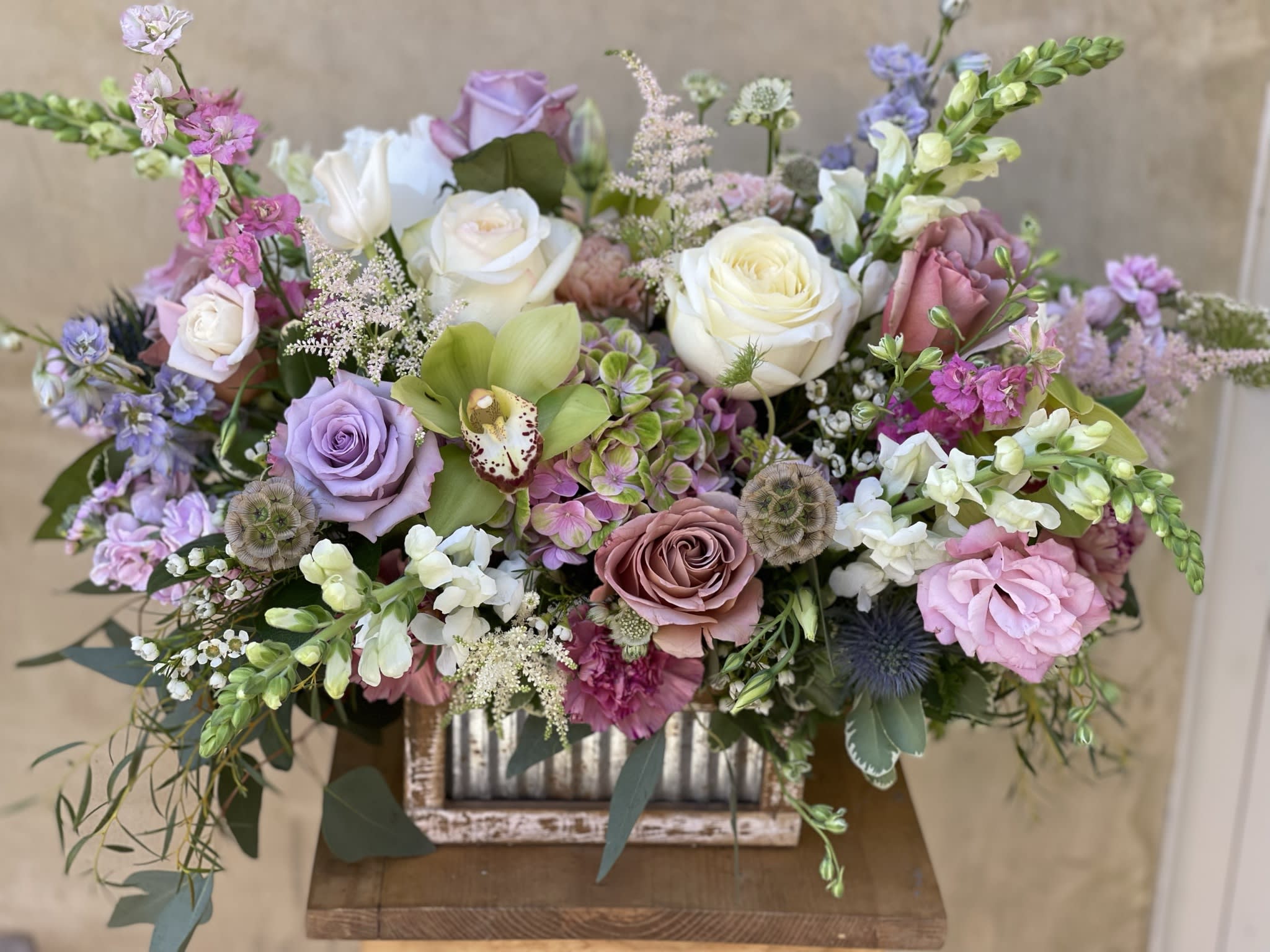 Mixed pastel bouquet with roses, orchids, and snapdragons in a rustic container