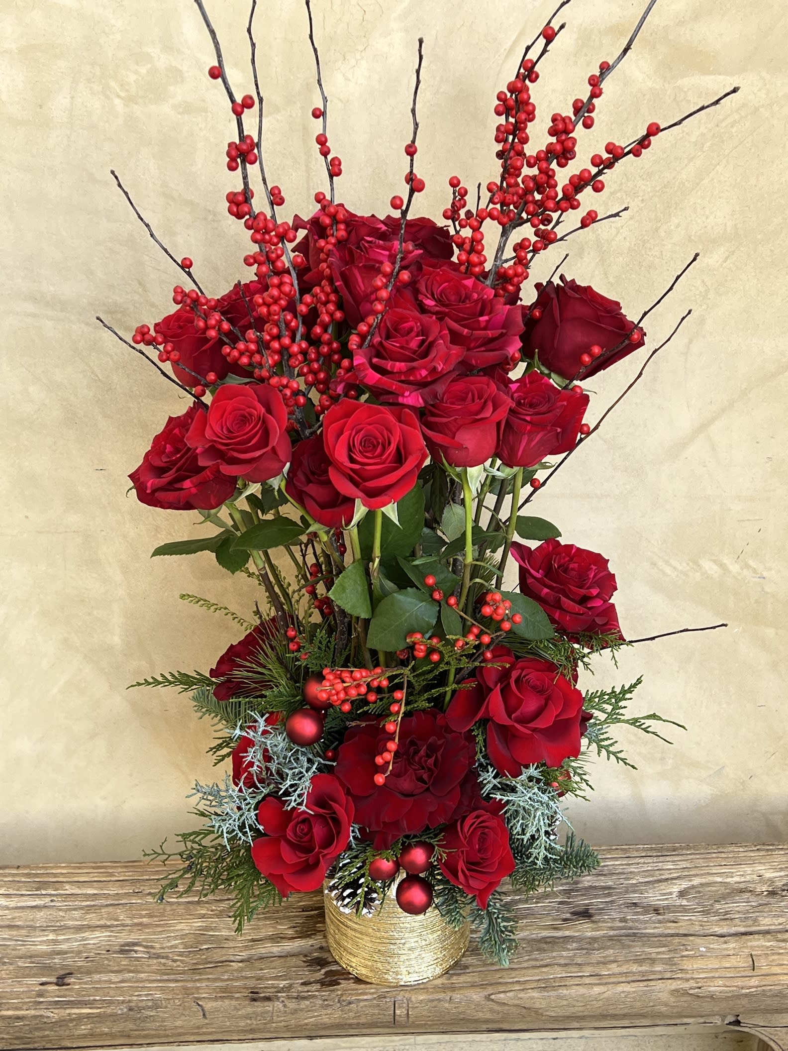 Tall arrangement of red roses with berry branches in a gold vase