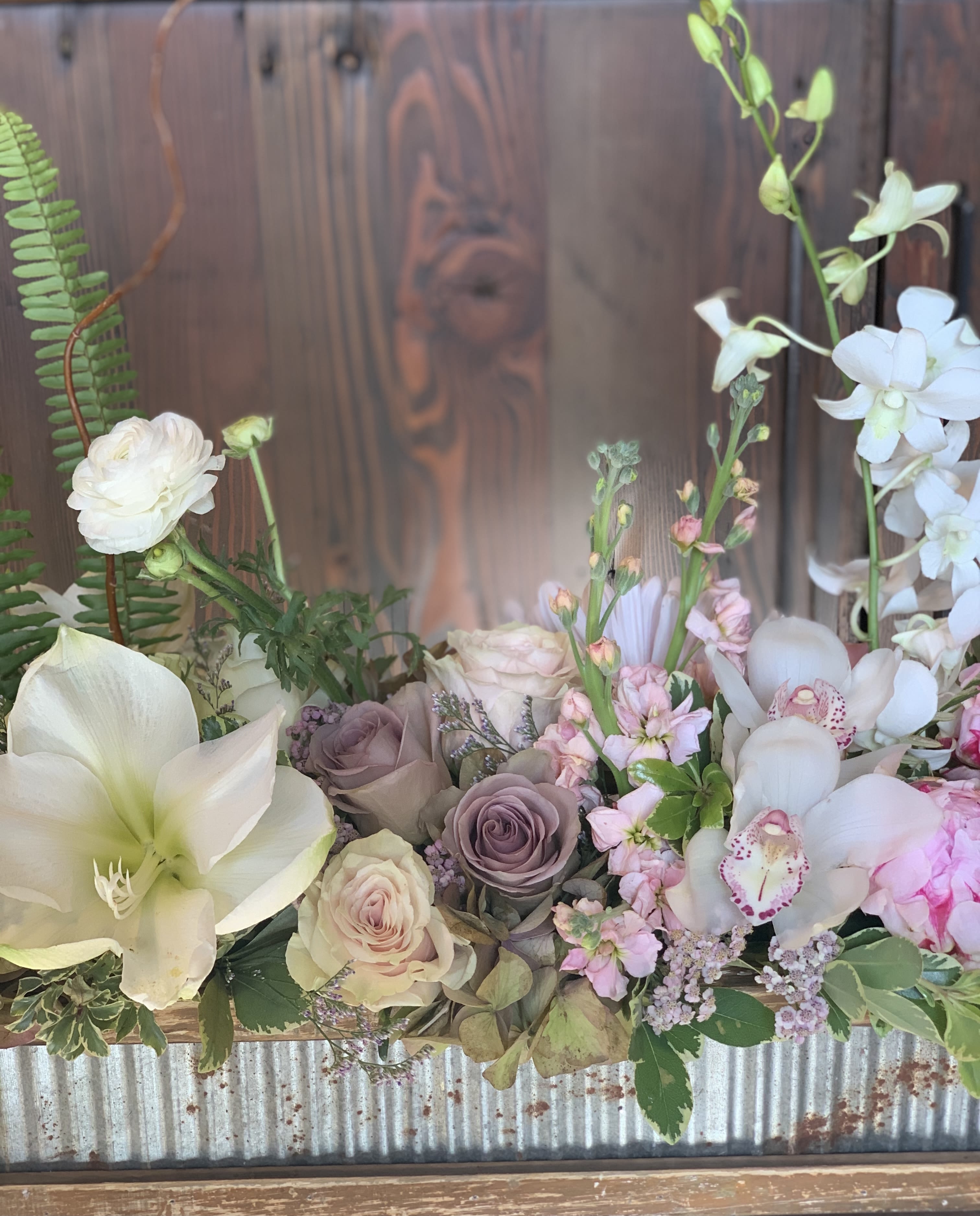 Pastel floral arrangement with white lilies, roses, and orchids in a rustic container