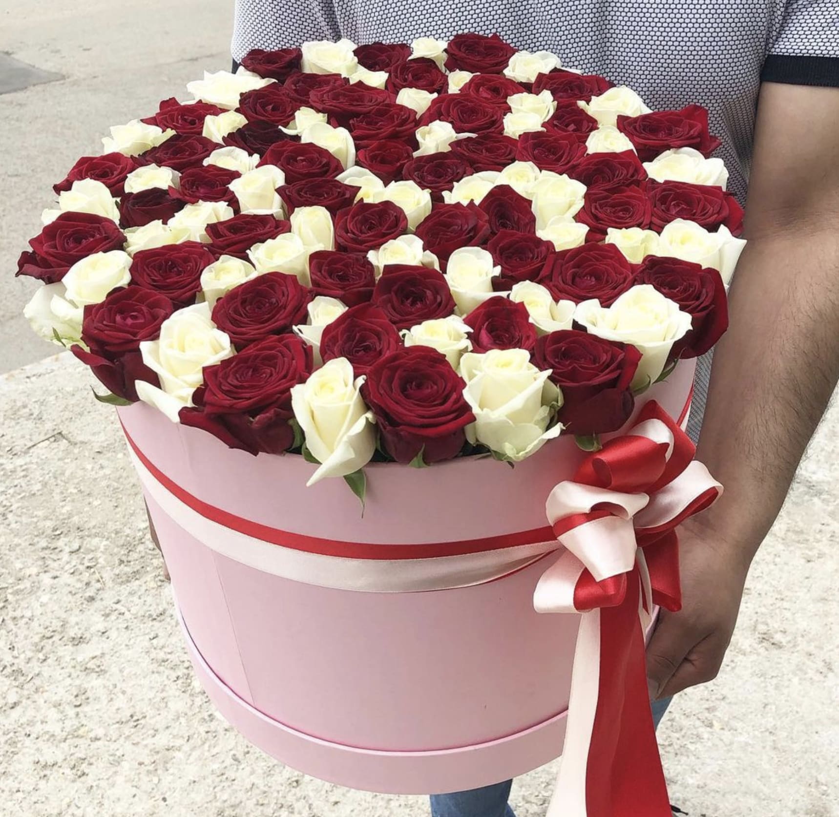 Round pink hat box filled with red and white roses and tied with red and white ribbons