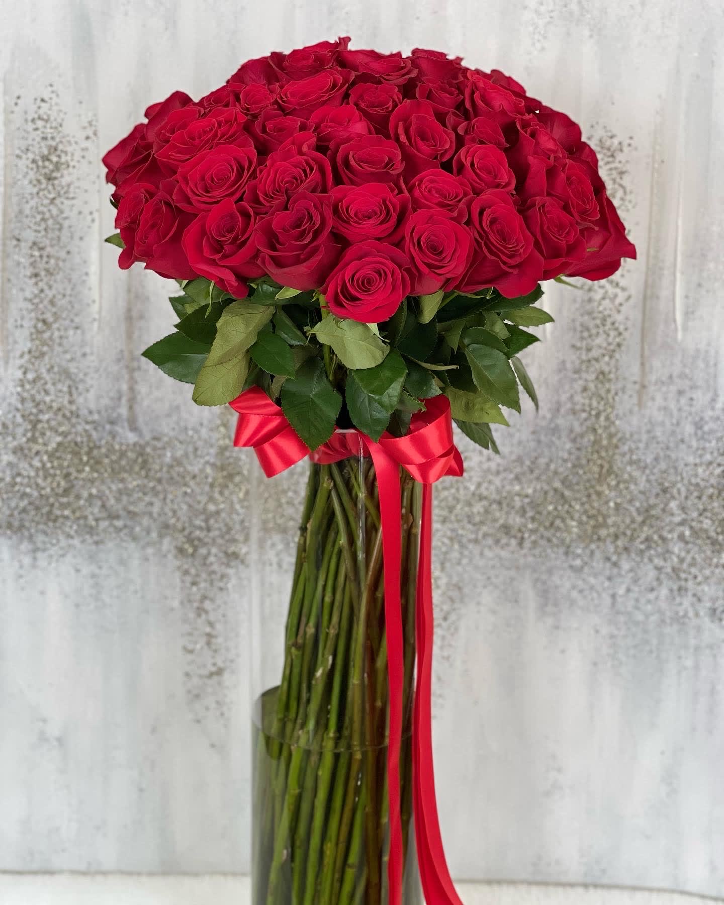 Tall bouquet of red roses in a glass vase with a red ribbon