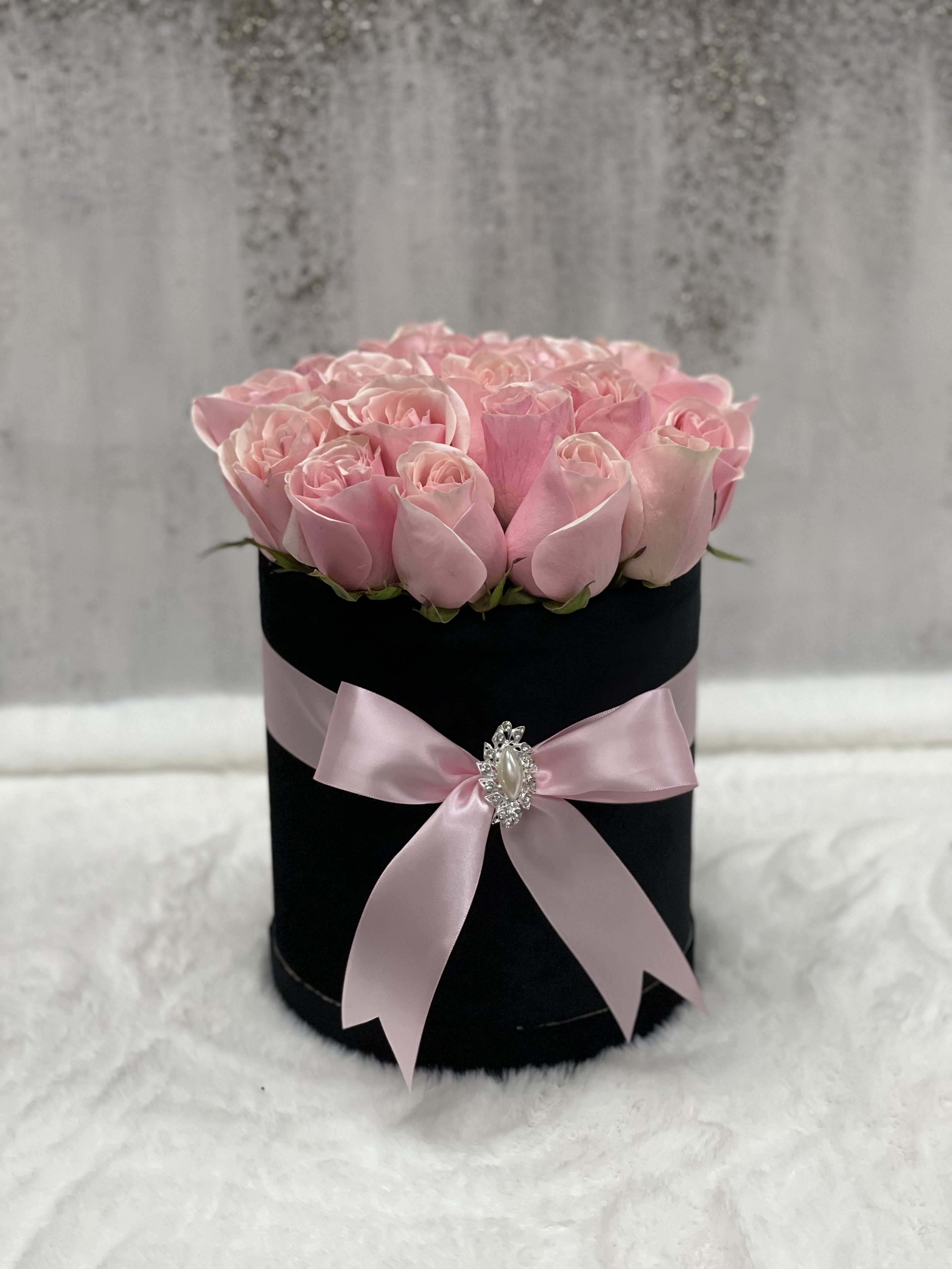Round black hatbox filled with light pink roses and tied with a pink satin bow.