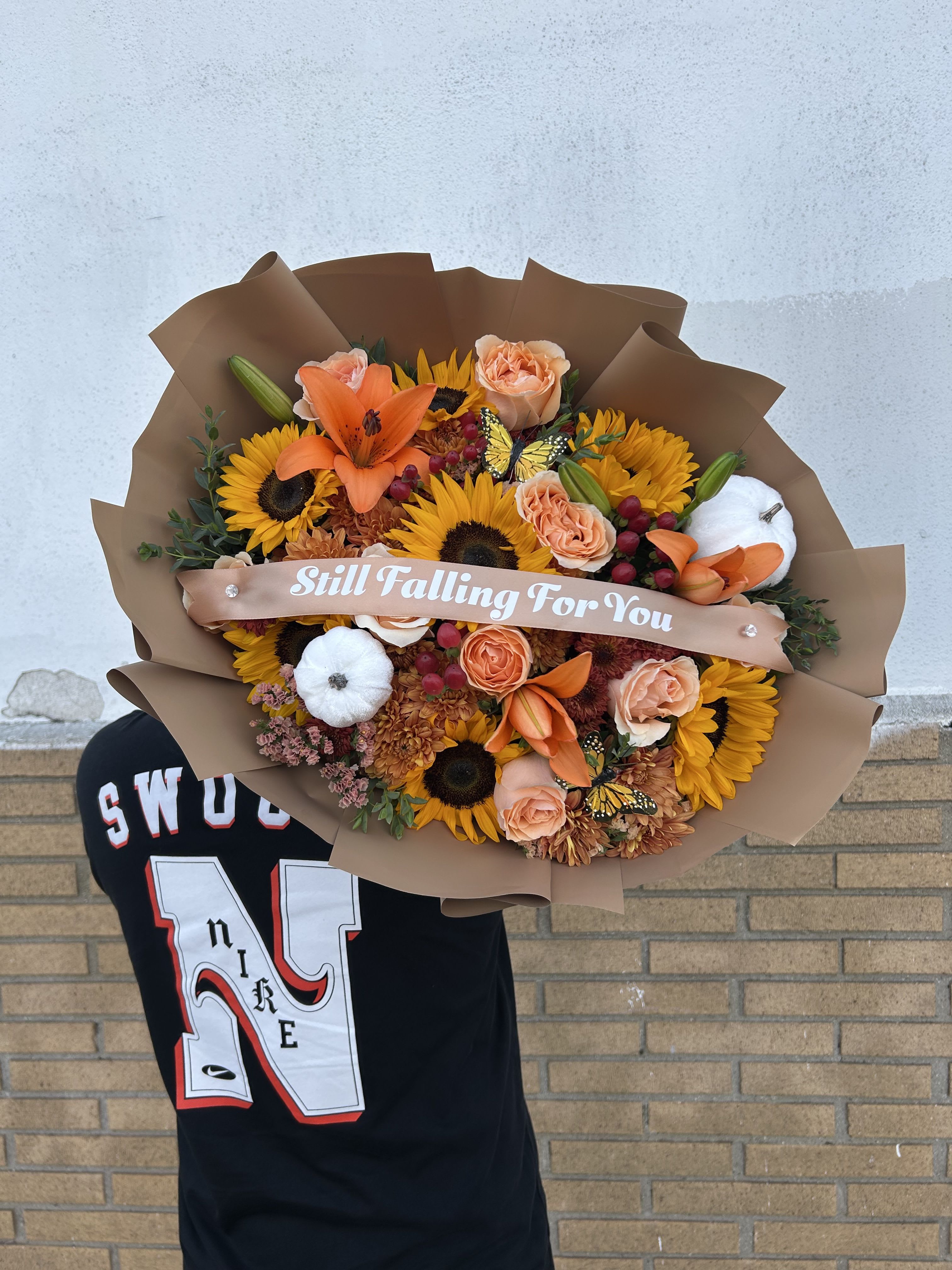 Bouquet of sunflowers, peach roses, and orange lilies wrapped in brown paper