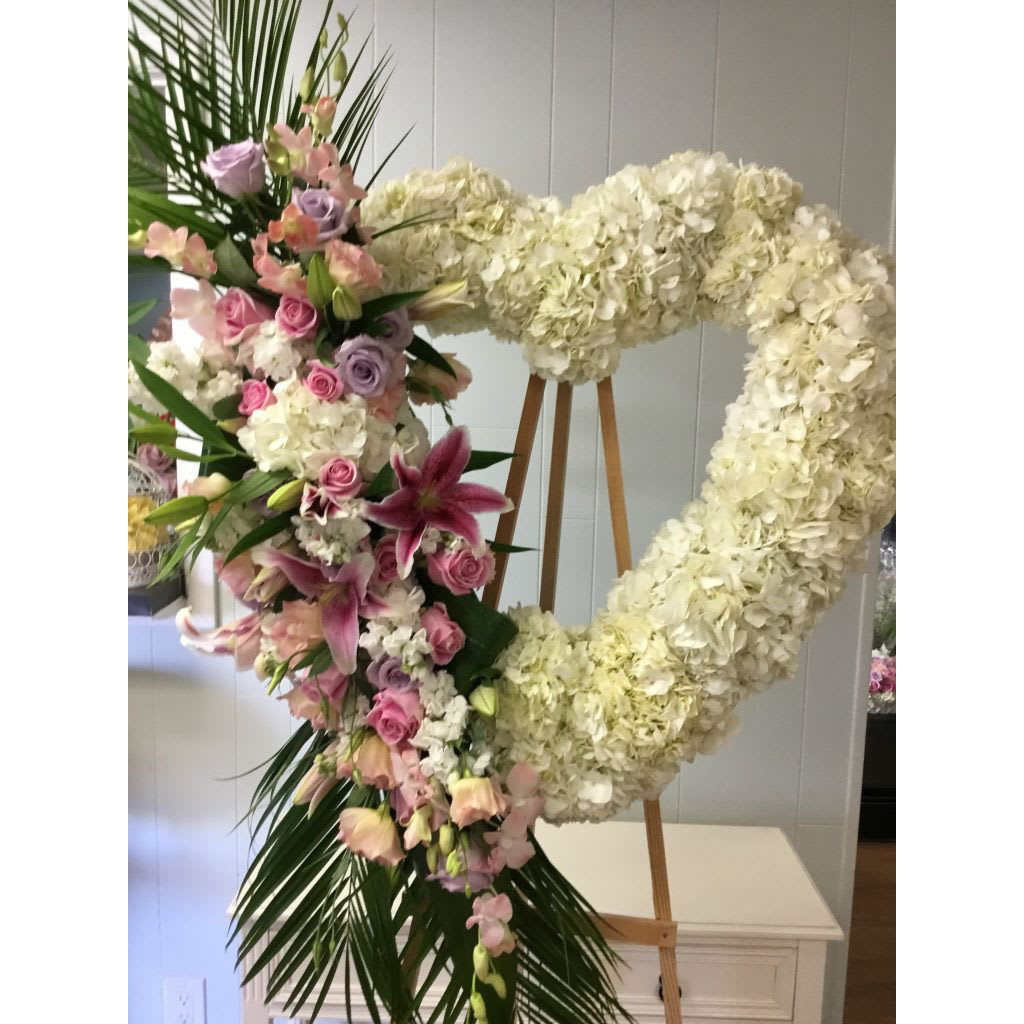 Heart-shaped floral wreath with white hydrangeas, pink roses, and lilies on an easel