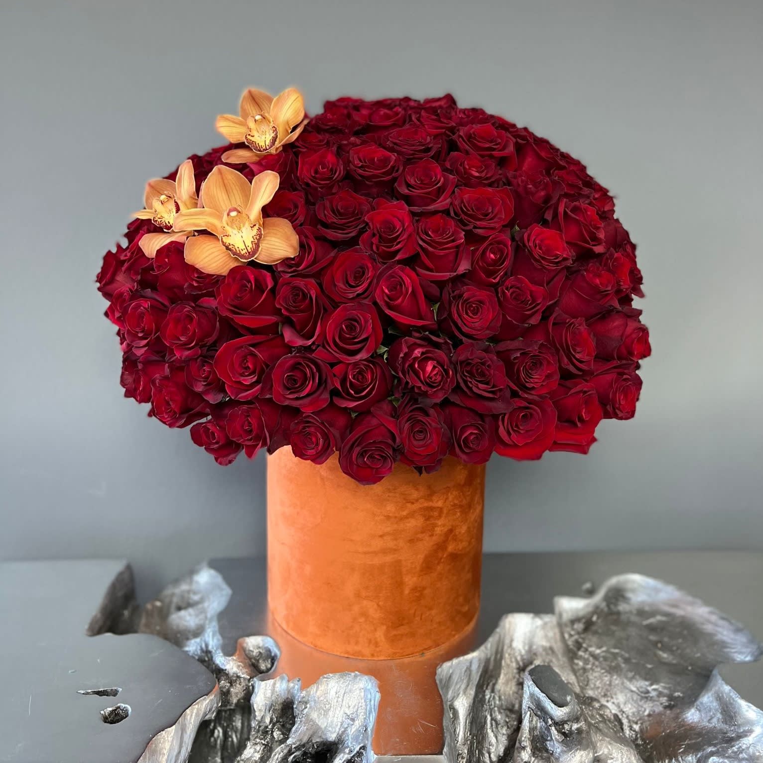 Red rose arrangement in an orange velvet vase with peach orchids