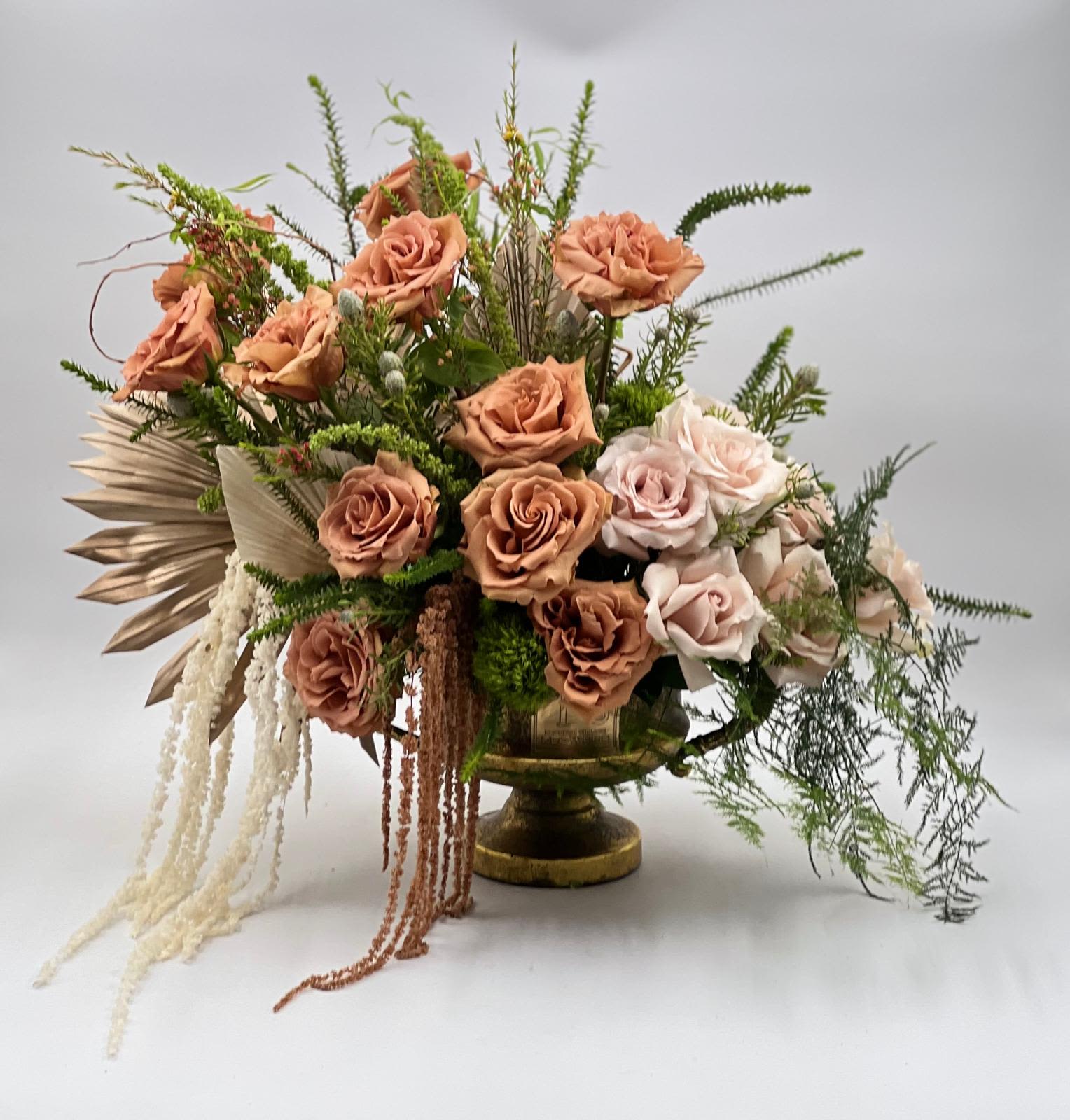 Golden Garden - This luxurious arrangement features warm mocha and blush roses, lush greenery, and cascading textures in an elegant gold pedestal vase. Designed with movement and depth, it brings a refined garden-style feel that is both graceful and timeless. A perfect expression of love and appreciation, this piece makes a stunning and memorable gift for someone truly special.