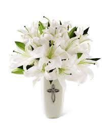 White lilies arranged in a tall white vase with a cross emblem