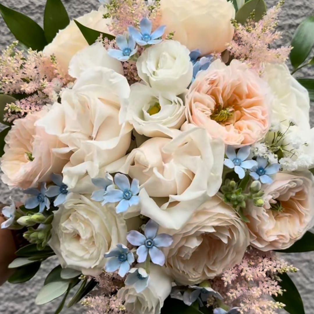 Wedding bouquet of cream and blush roses with small blue flowers