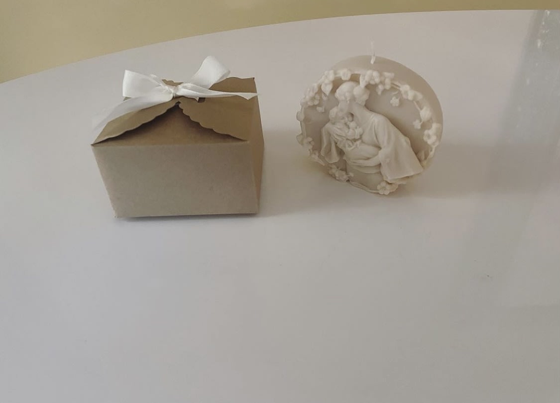 A small kraft gift box with a white ribbon beside a white decorative figurine.