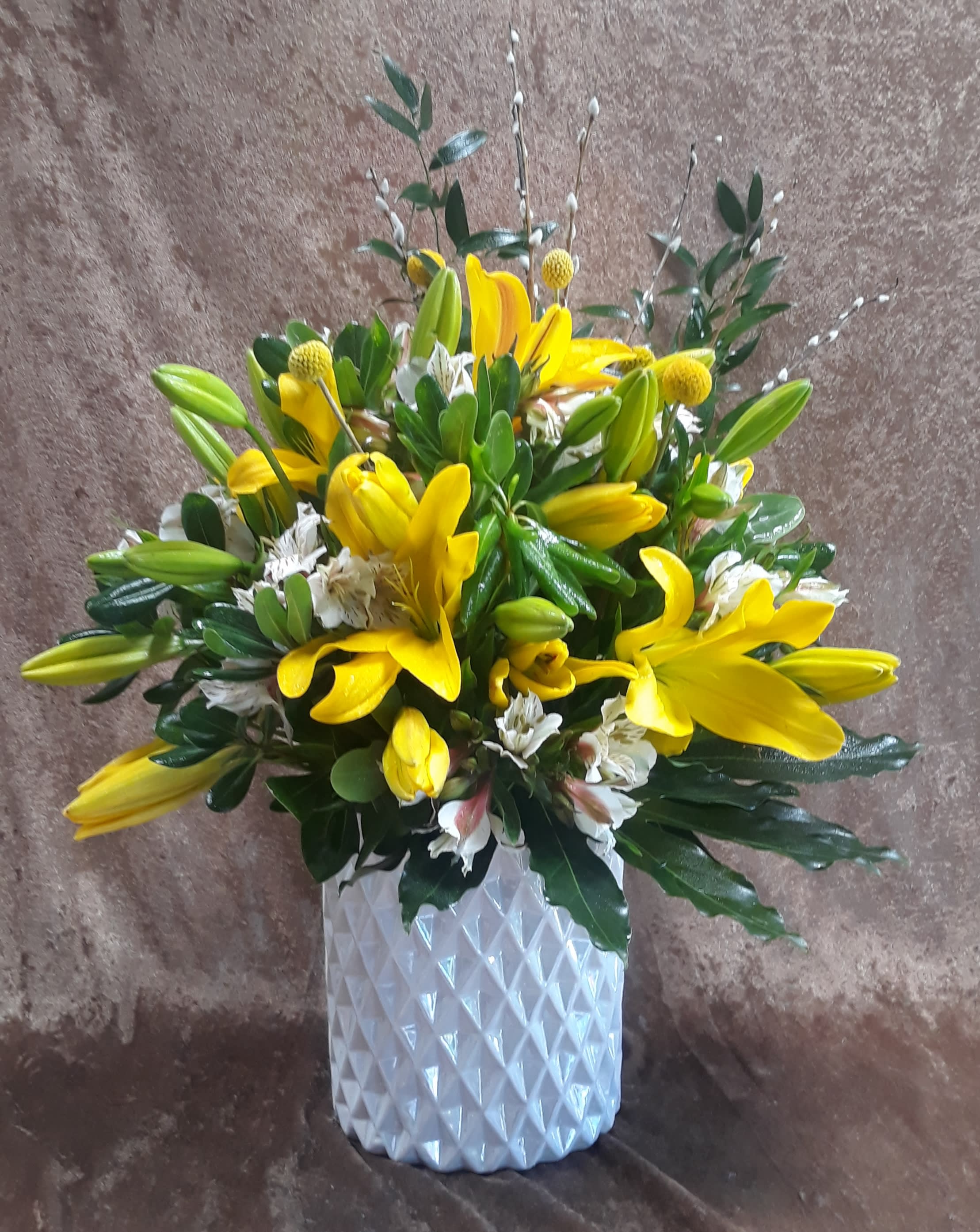 Yellow lilies and white flowers arranged in a white textured vase
