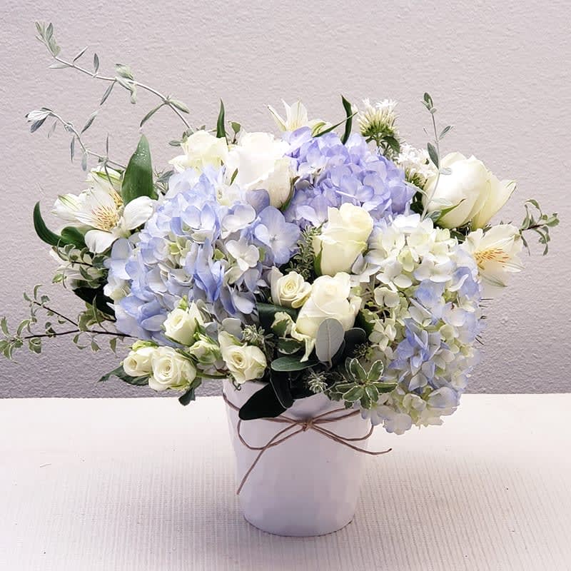 White and pale blue flowers arranged in a white vase.