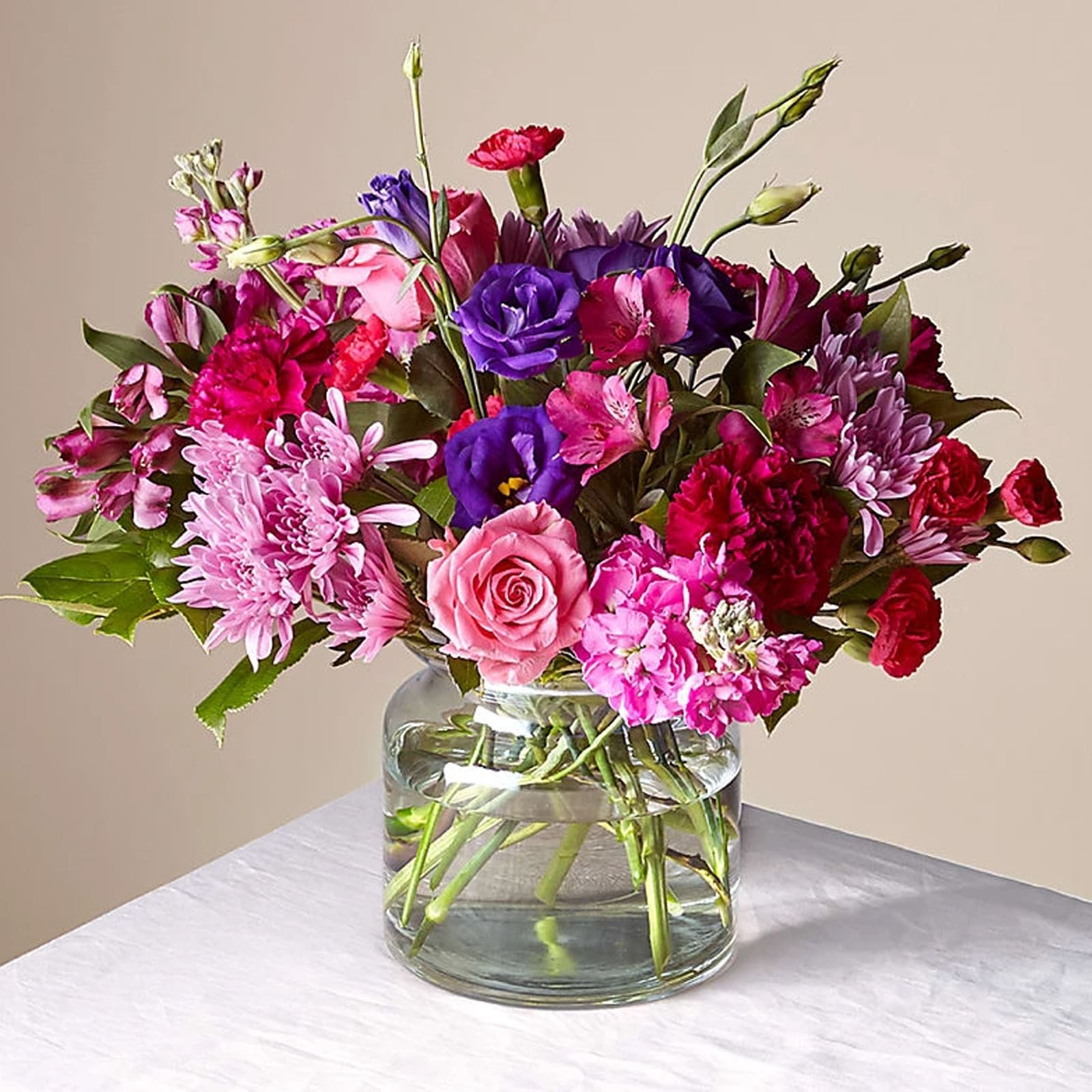 Sweet Thing Bouquet - Bursting with vibrant hues, this bouquet is a vivid tapestry of fuchsia, pink, and purple flowers. It features an array of blossoms including lush roses, striking lisianthus, and ornate chrysanthemums, all artfully arranged in a clear, round vase.   How sweet to remind your Galentine, mom, or someone special that you love them with this beautiful bouquet.  Approximately 11" H x 15" W. 