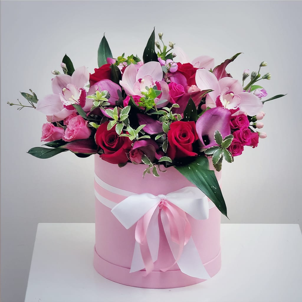 Luxe Pink Gift Box Bouquet - Capture the moment's beauty with our Luxe Gift Box Arrangement. Our flower stylists finish this arrangement in a round hat-box with a combo of spry rose, cymbidium orchids, and seasonal blooms and accents.   This breathtaking arrangement is a lovely and luxurious gift for your loved ones.  For long-lasting flowers, add water daily to keep the oasis moist.  Approximately 18" H x 16" W.  