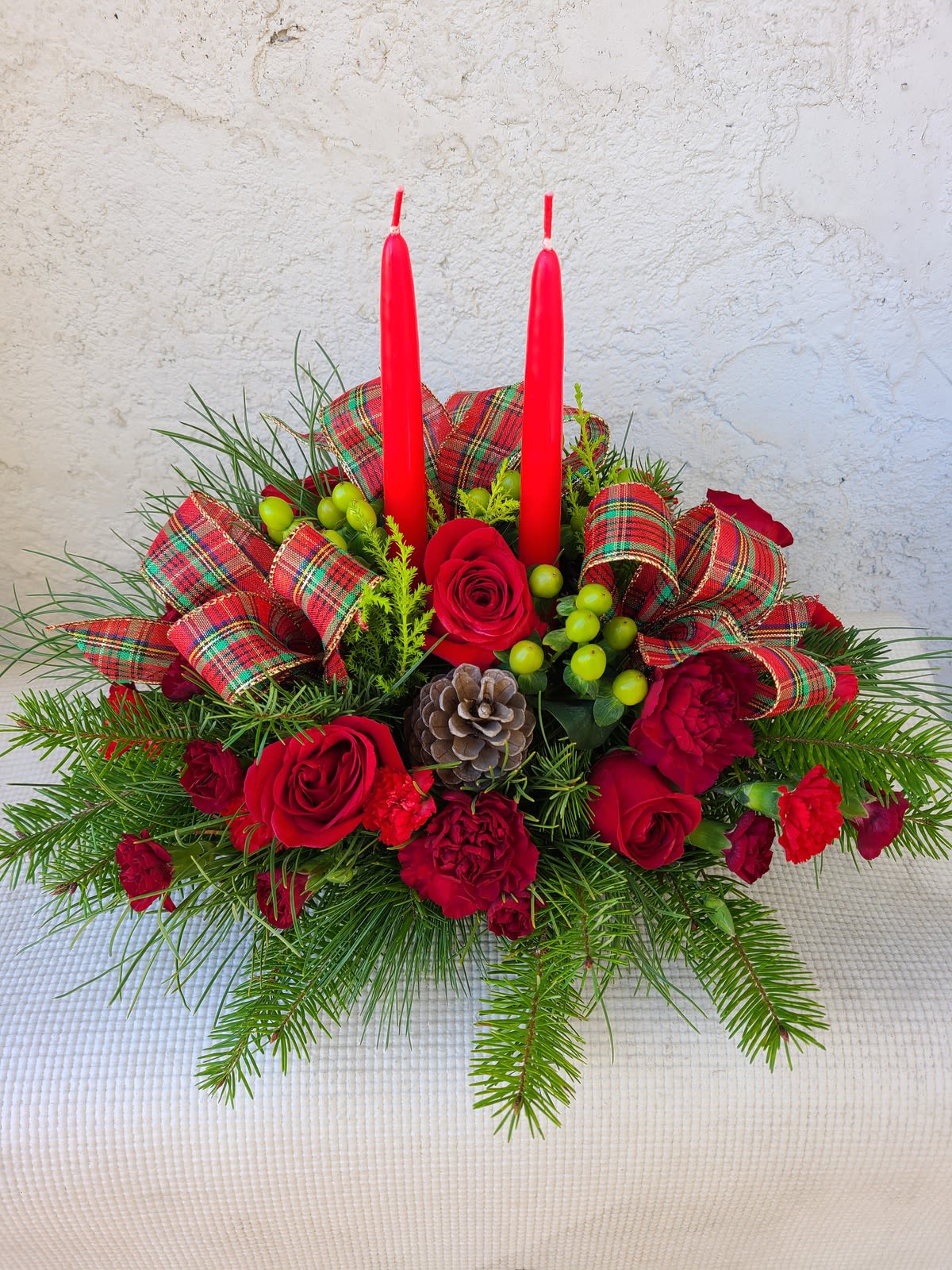  I’ll be Home for Christmas - Your loved ones will be feeling merry and bright when they receive this centerpiece. With roses, carnations, hypericum berries, and Christmas greens, vibrant red blooms make a bold statement with your holiday decor. Approximately 7 "H x 18" W.