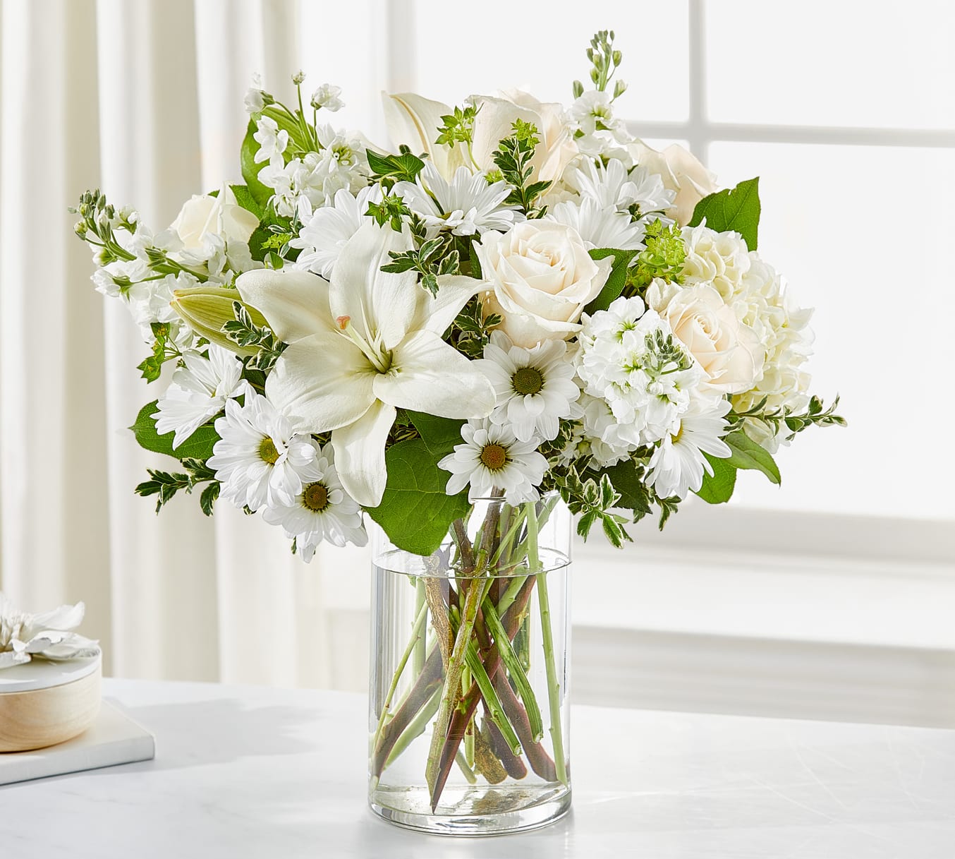 White roses, lilies, and daisies arranged in a clear glass vase