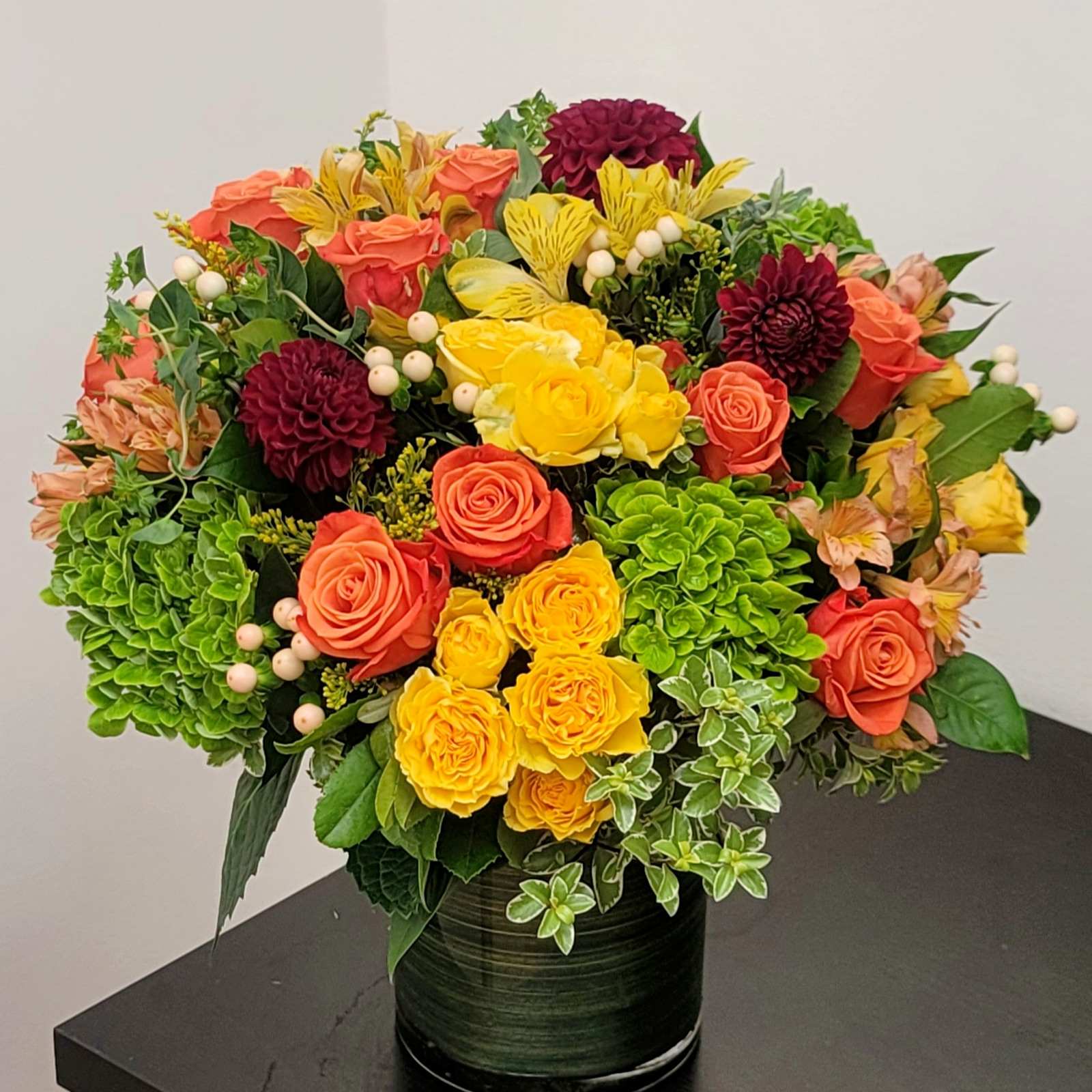 Colorful bouquet of roses, dahlias, and hydrangeas in a dark vase