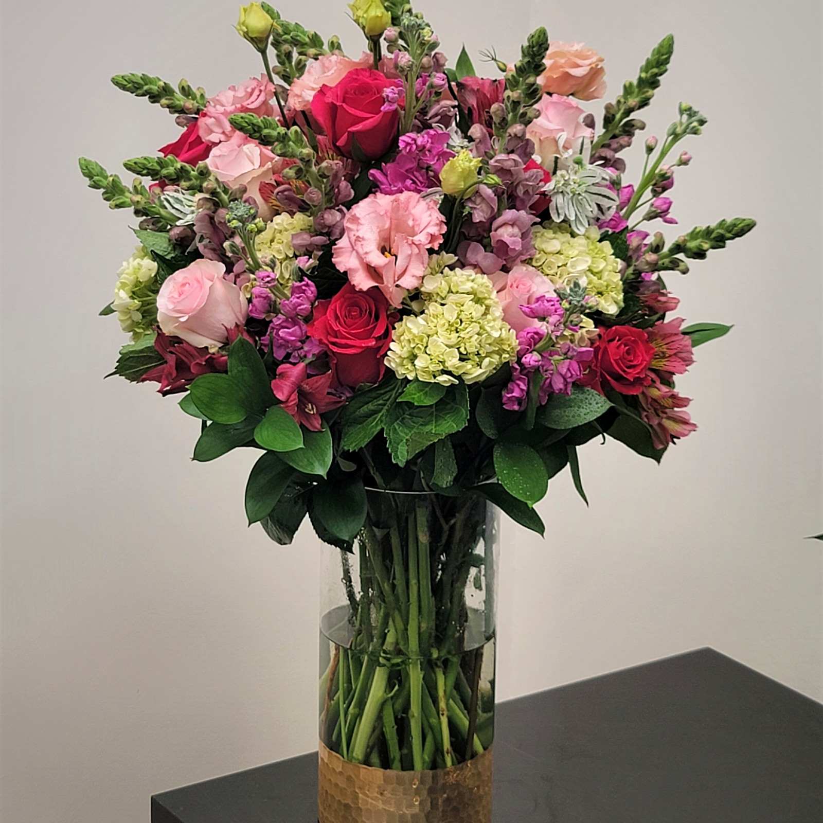 Mixed pink and red flowers arranged in a tall glass vase