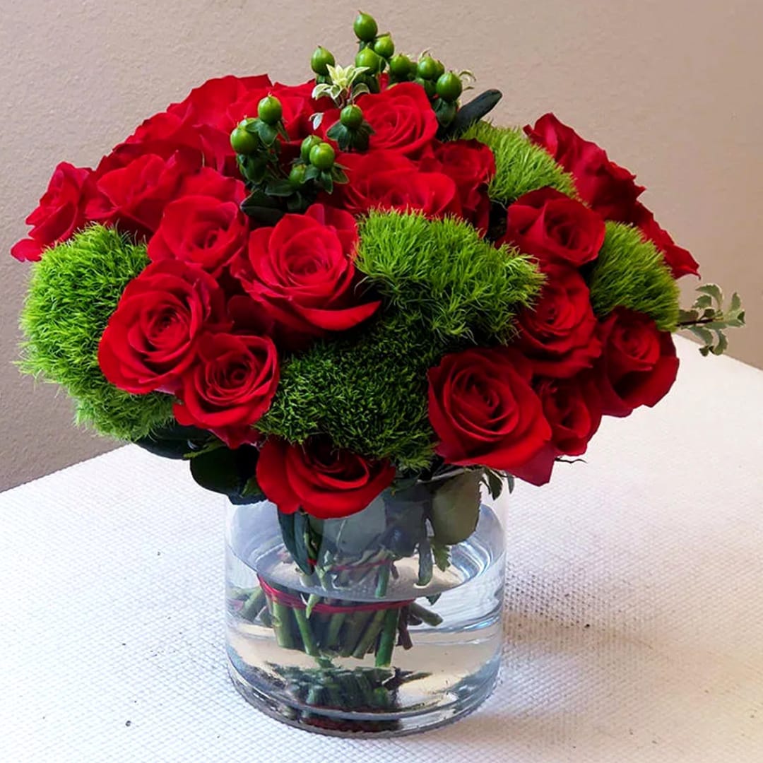 Red roses arranged in a clear glass vase with green filler accents