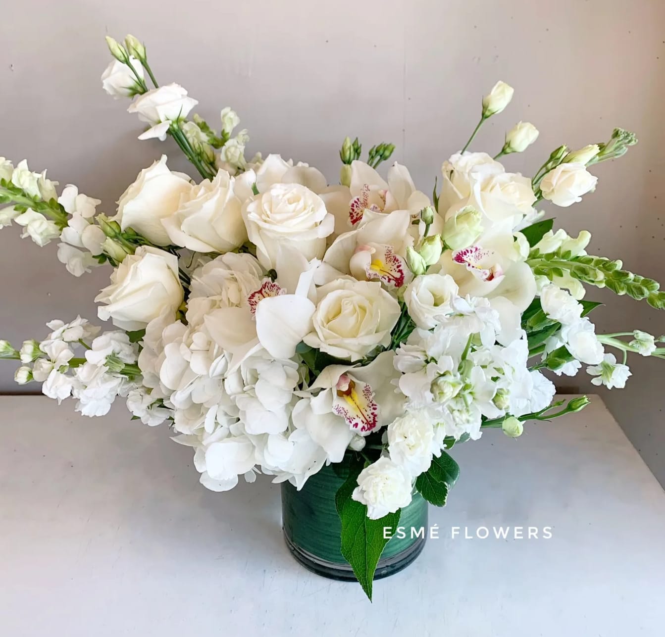 White floral arrangement in a green vase with roses and orchids