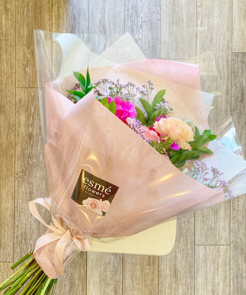 Pink and peach bouquet wrapped in translucent paper with a ribbon
