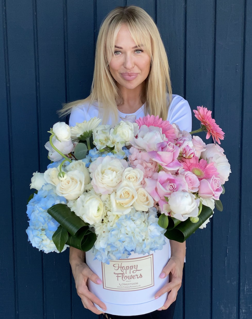 Woman holding a large hatbox arrangement of pink, white, and blue flowers
