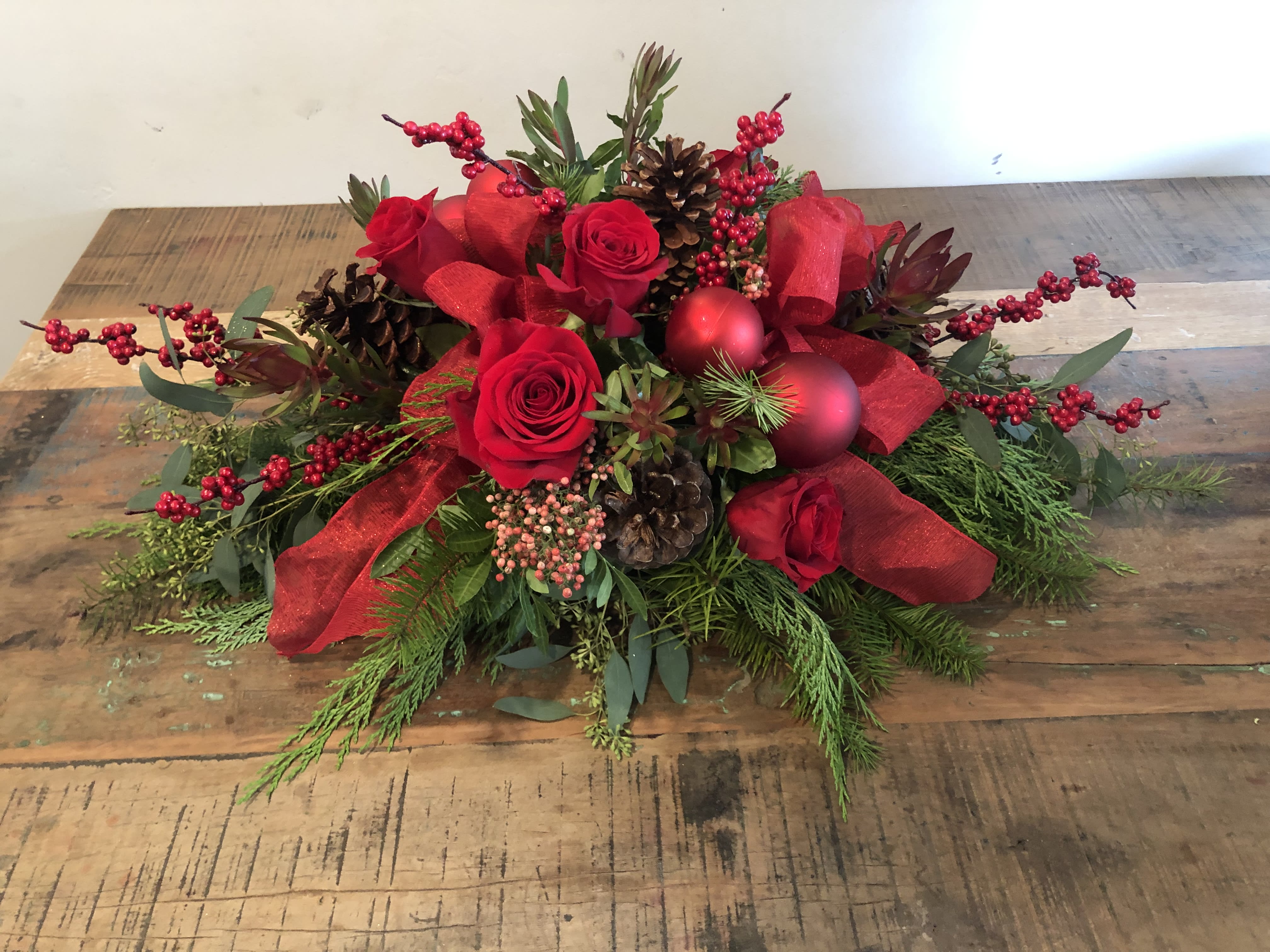 Red roses with pinecones, berries, and ribbon in a low holiday arrangement