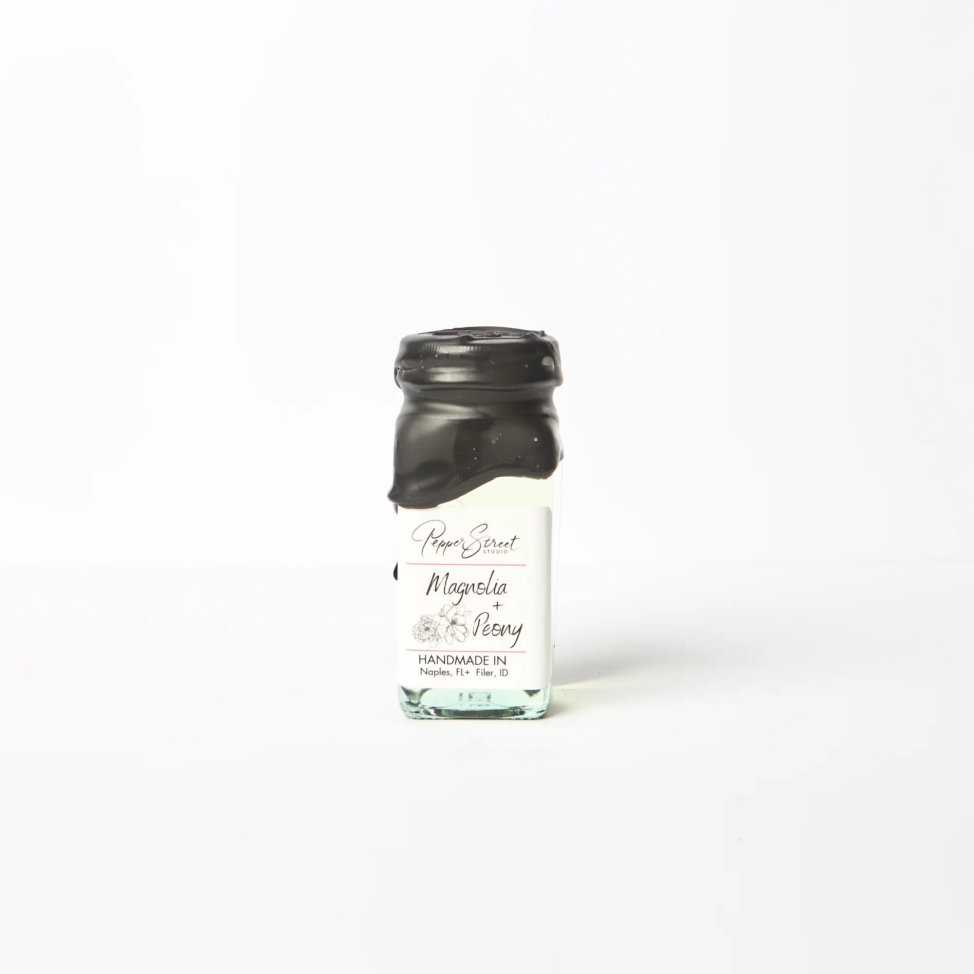 MAGNOLIA + PEONY MINI ROOM DIFFUSER - Pepper Street's signature black wax and hand-dipped room diffuser, in a square glass bottle. It includes ten bamboo reeds and a wood flower for a sweet touch and effective scent diffusion. Their diffuser oils are wholly toxin-free and contain no additional alcohol, ensuring a long-lasting scent that will last you longer than eight months. A pull tab on the back allows easy access to the lid.  Bottle size: 4 fluid ounces. Magnolia + Peony Immerse yourself in the refreshing scent of a blossoming spring garden with this exquisite blend of floral fragrances. The crisp and breezy magnolia notes are perfectly balanced with a hint of sweetness from the peony, creating a delicate aroma that's sure to revitalize and calm any space in your home. Whether you have a love for all things floral or simply want to add a touch of tranquility to your living space, this fragrance is guaranteed to delight. Linen gift bag included.
