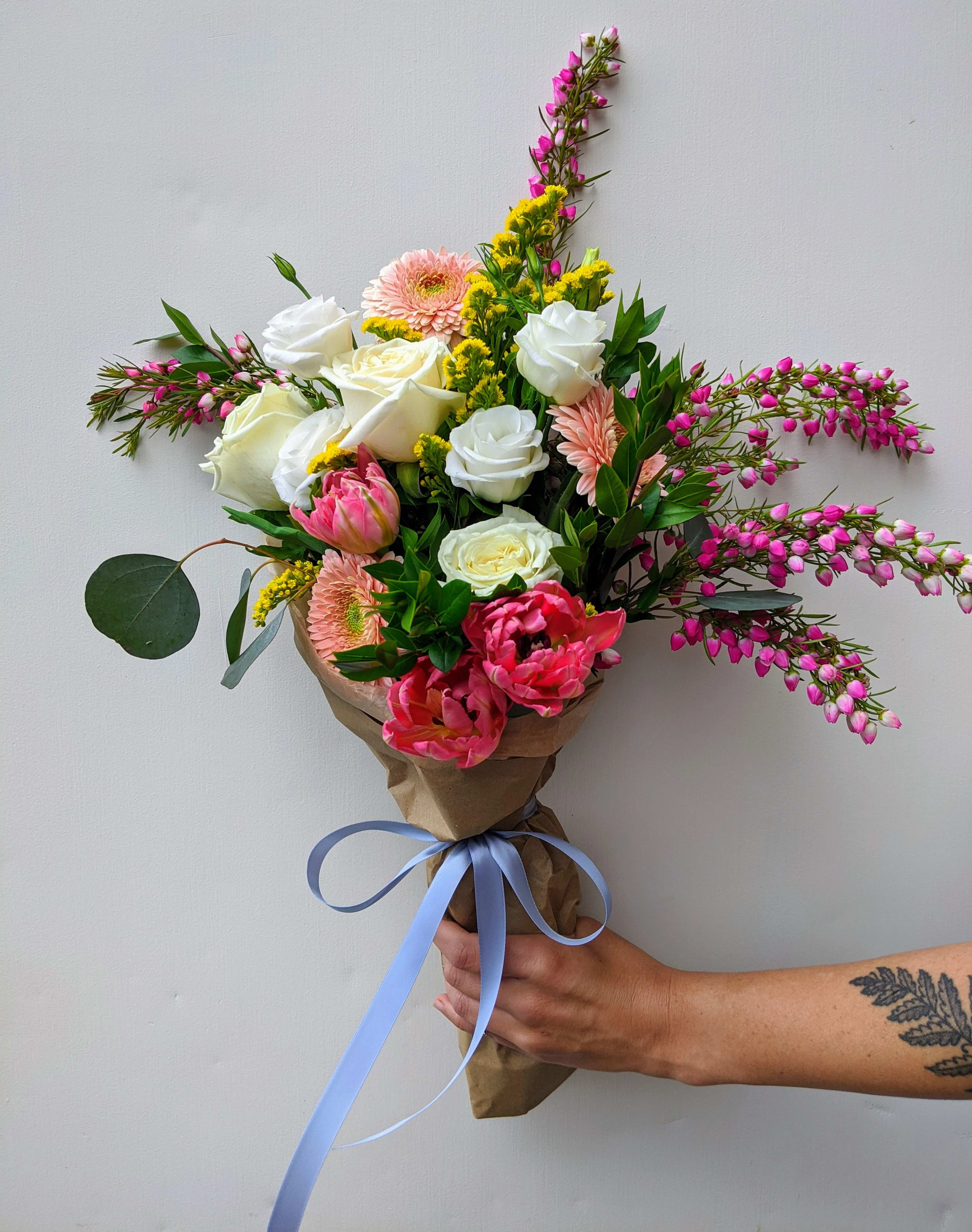 Hand-tied bouquet of white and pink flowers wrapped in brown paper with a blue ribbon