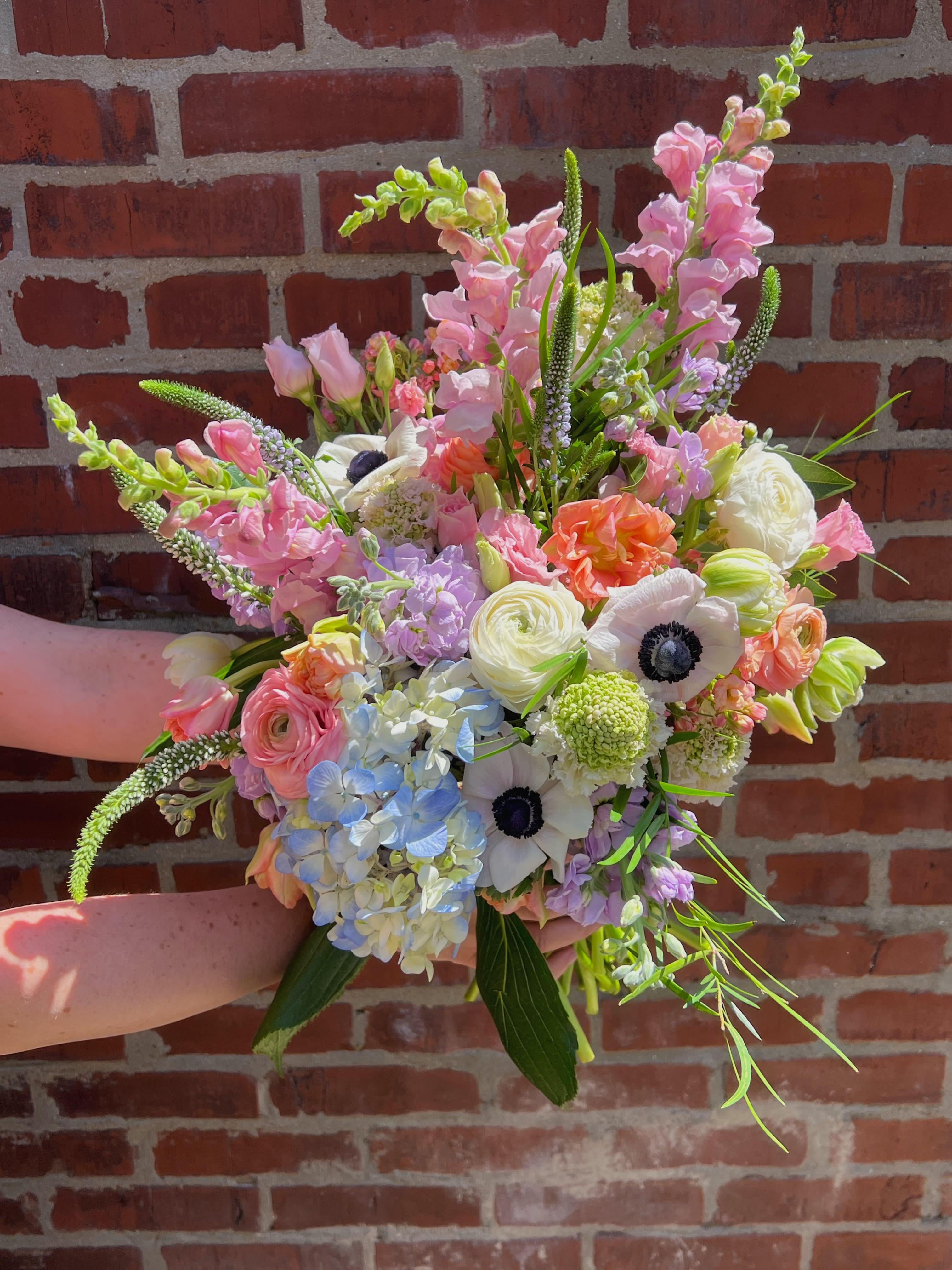Handheld bouquet of pastel pink, white, blue, and peach flowers