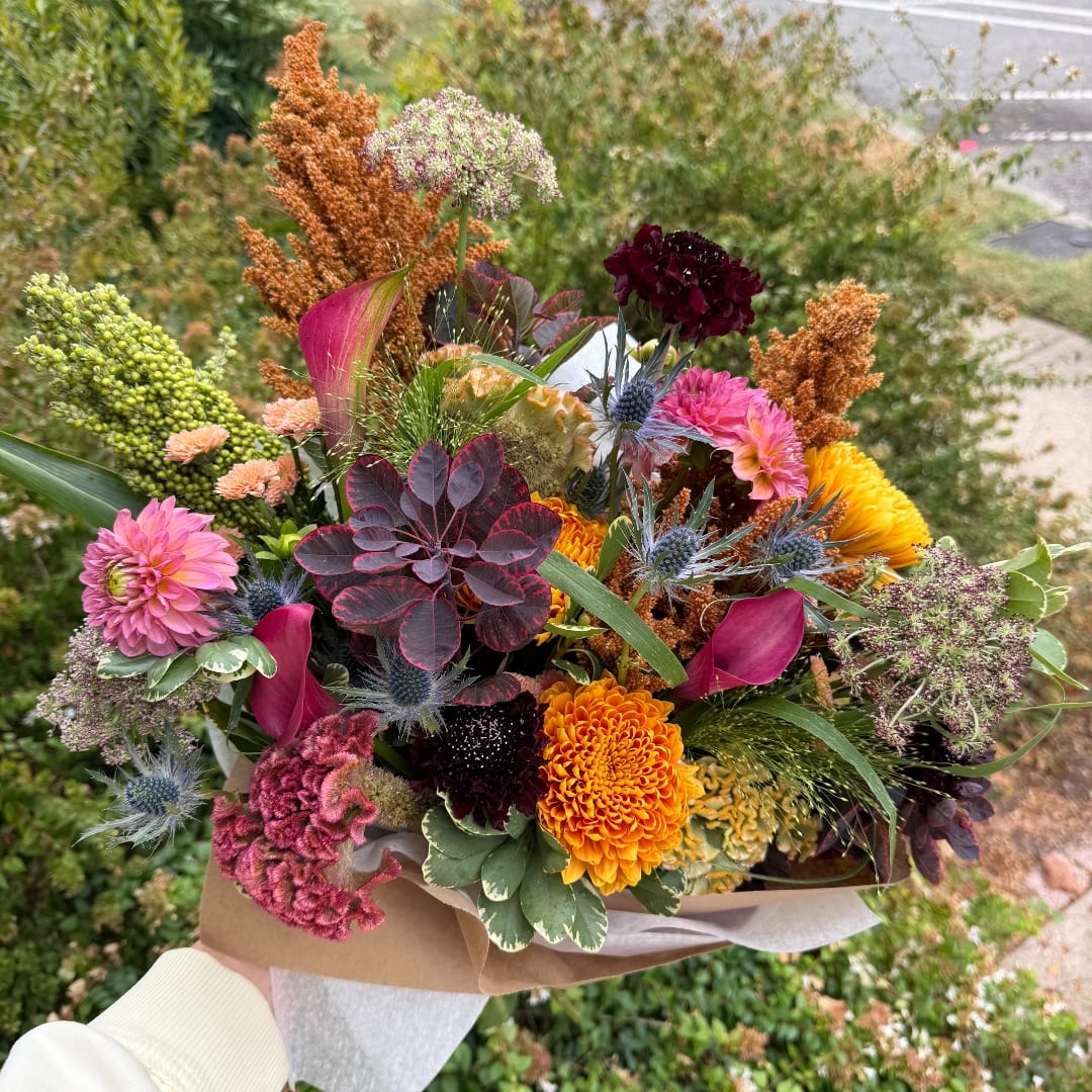 Handheld bouquet with pink, orange, yellow, and burgundy flowers
