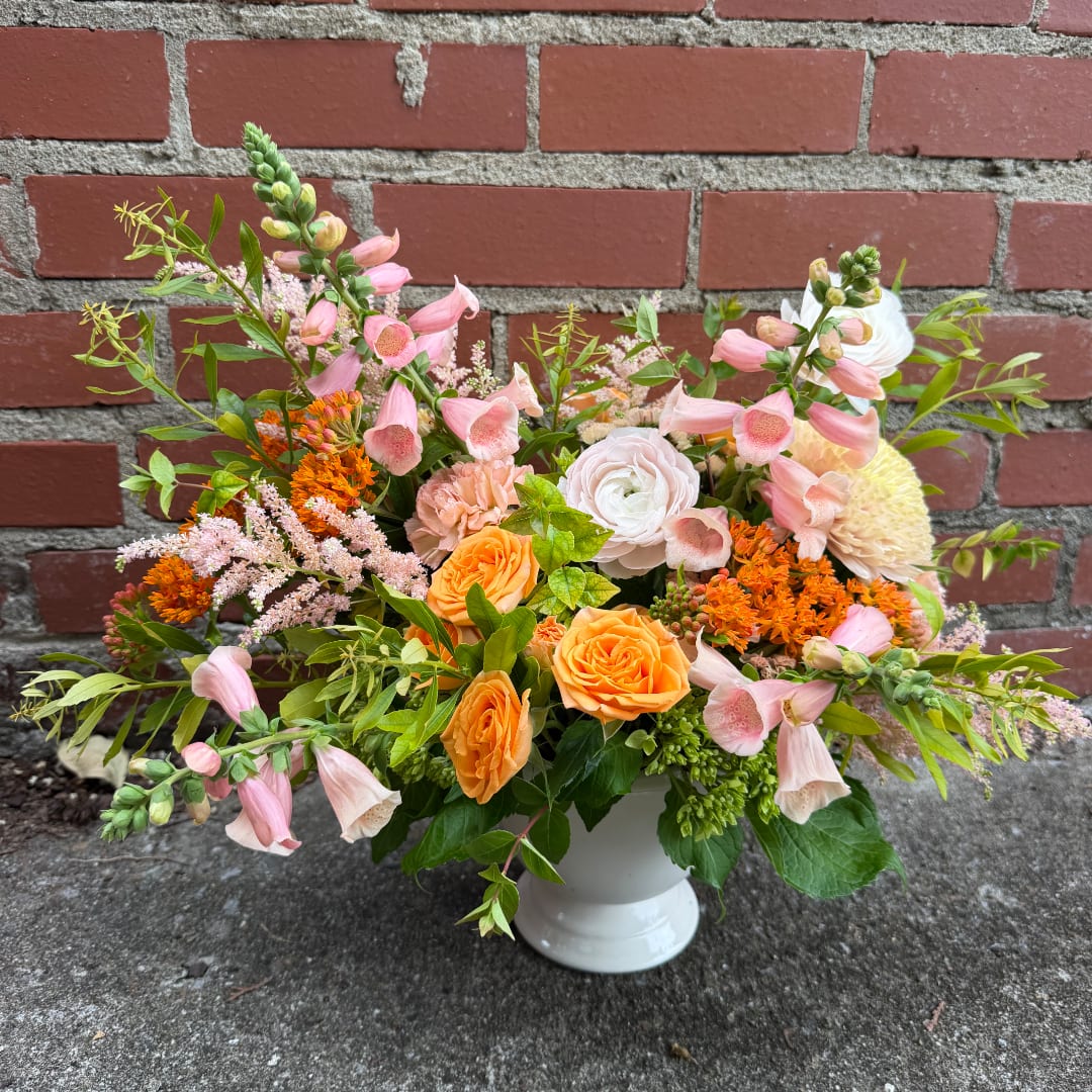 Mixed bouquet of pink foxglove, orange roses, and white blooms in a white vase.