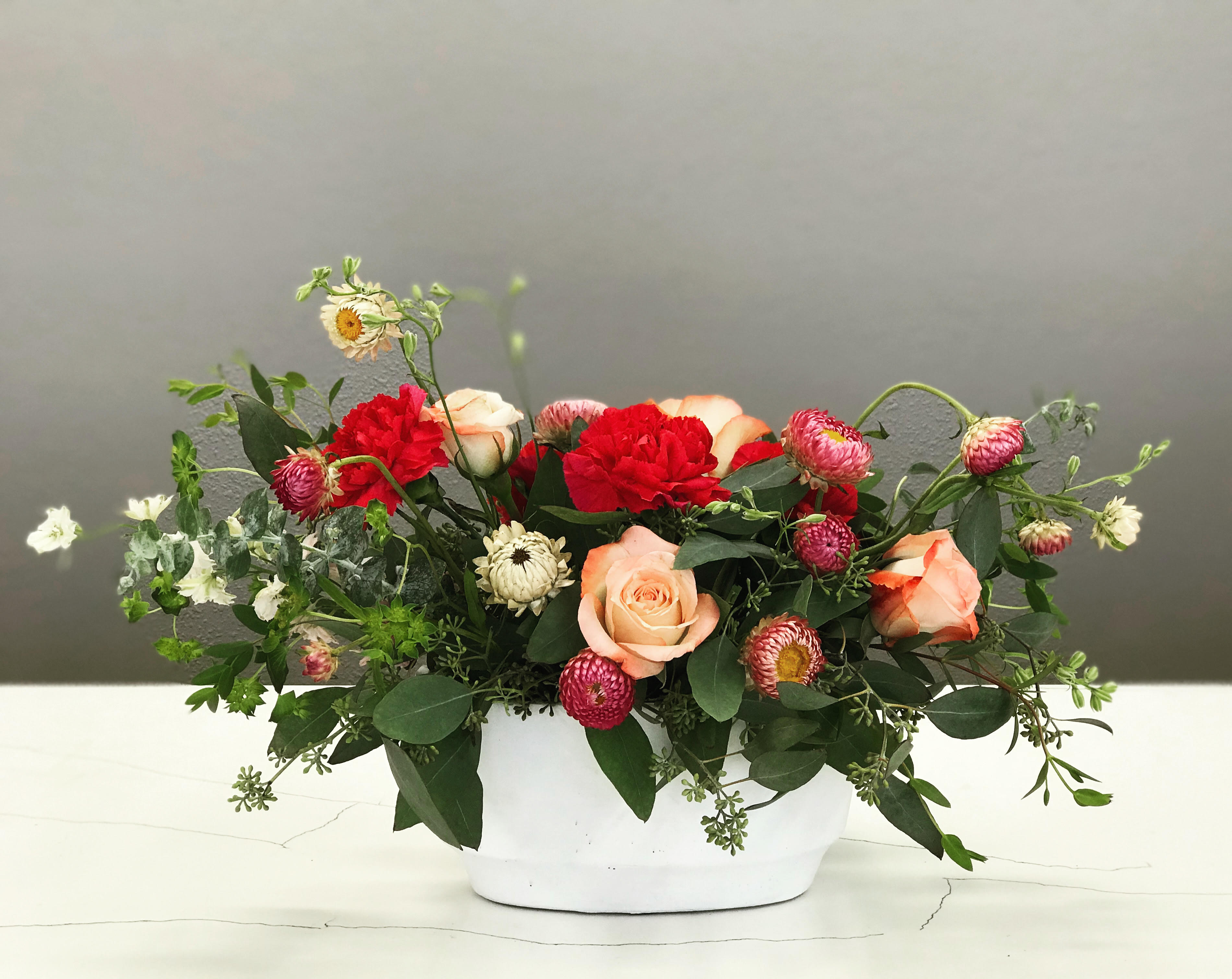 Mixed bouquet of roses and red carnations in a white container