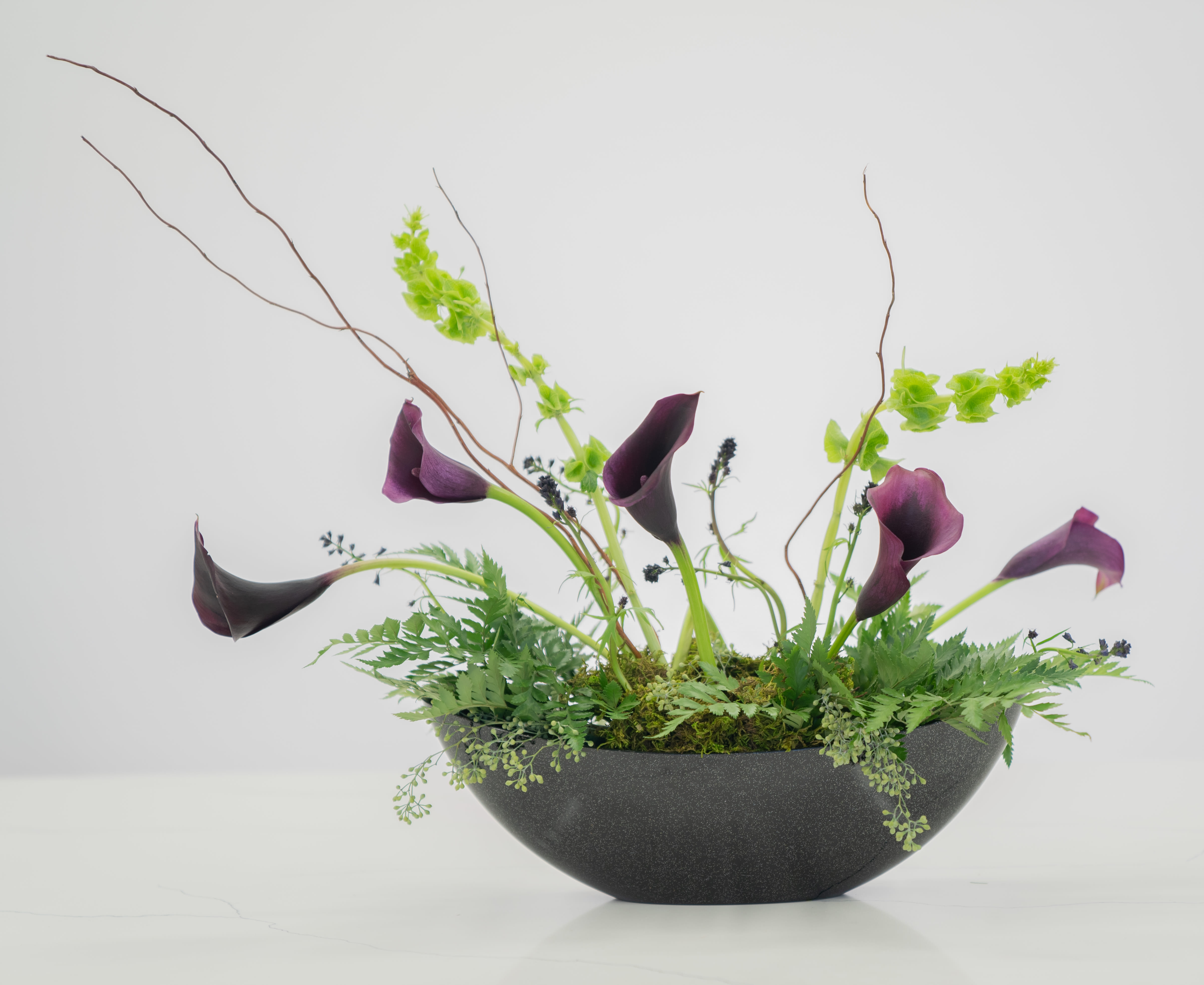 Purple calla lilies arranged in a black bowl with airy branches