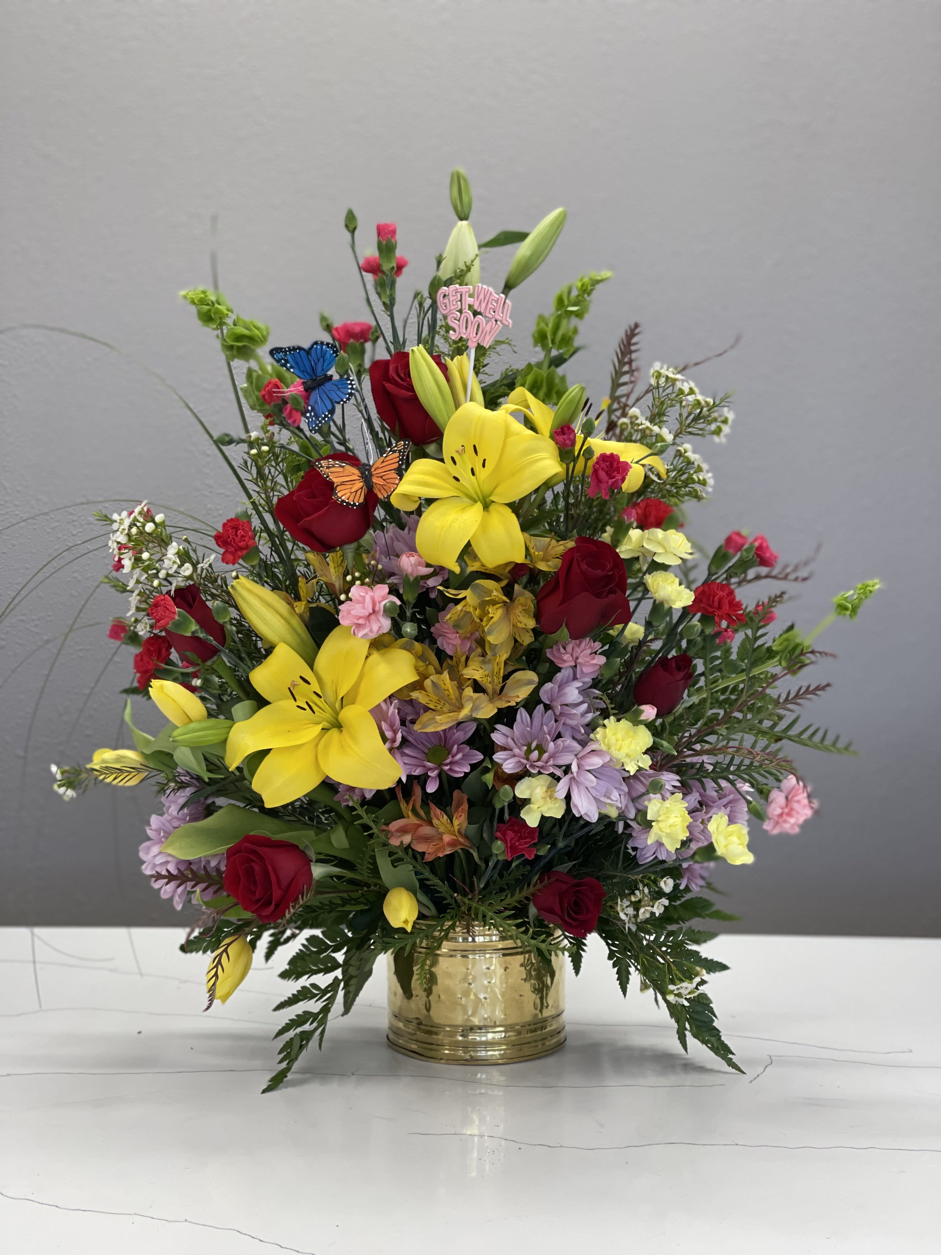 Mixed bouquet with yellow lilies, red roses, and a gold vase