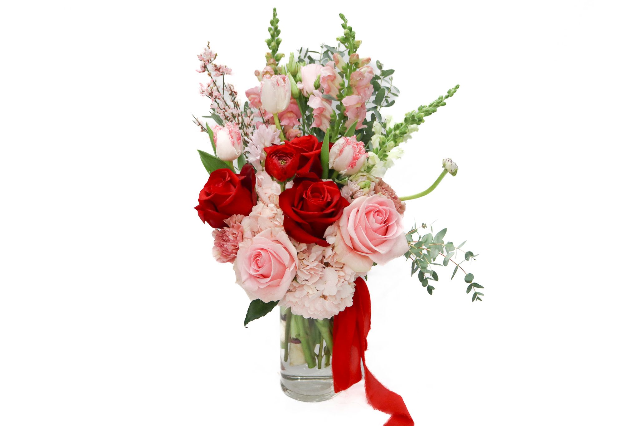 Red and pink roses in a clear glass vase with a red ribbon