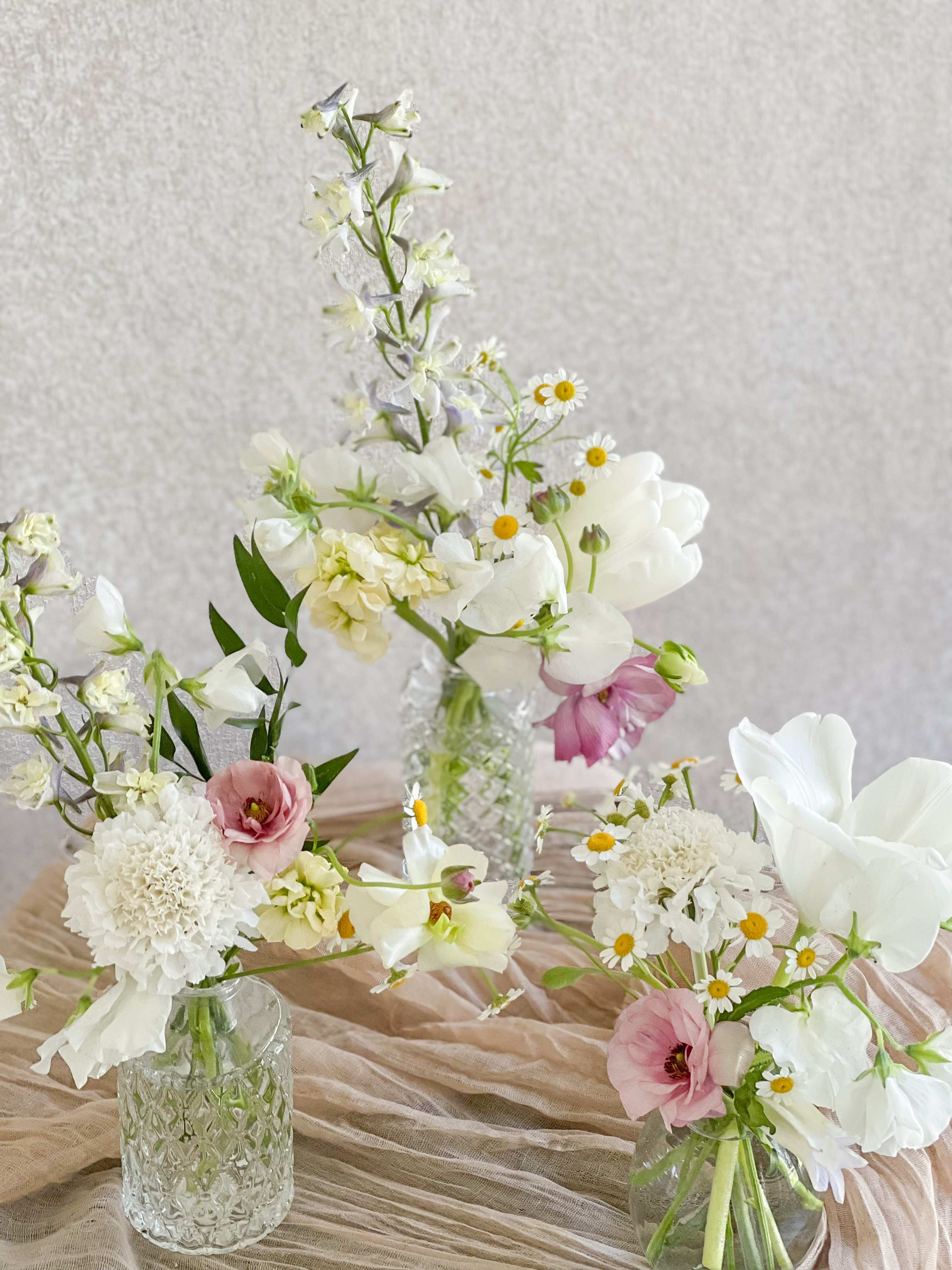 Three small floral arrangements in glass vases with white and pink blooms