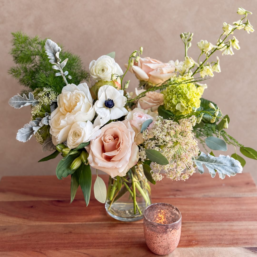 Mixed bouquet of pale roses and white blooms in a glass vase with a candle nearby